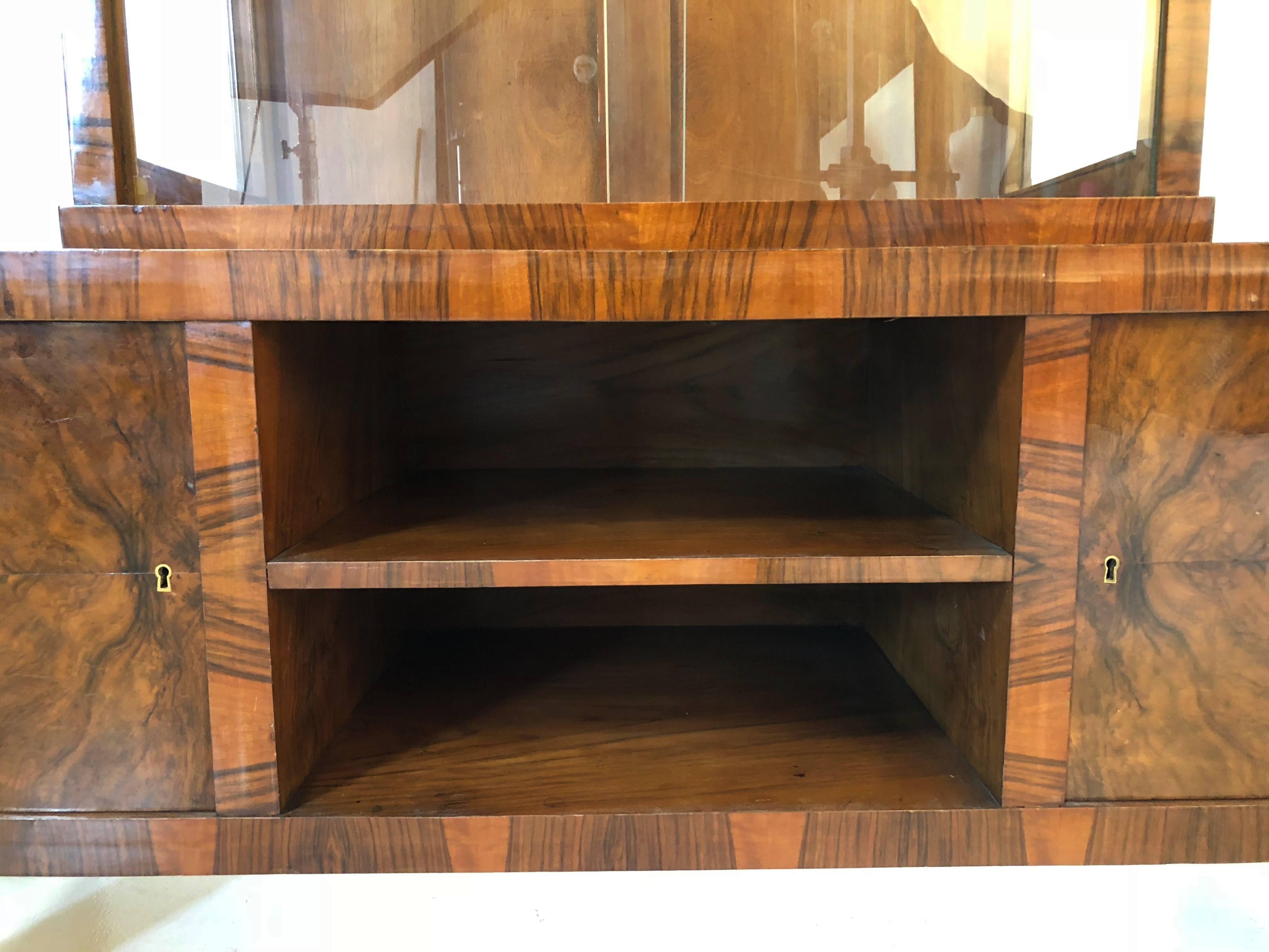 Beautiful Art Deco display cabinet, circa 1930. This elegant two-piece cabinet features a tall glass display case with sliding doors for curated art objects and books. Below this is a shelving unit flanked by doors with brass hinges and escutcheons