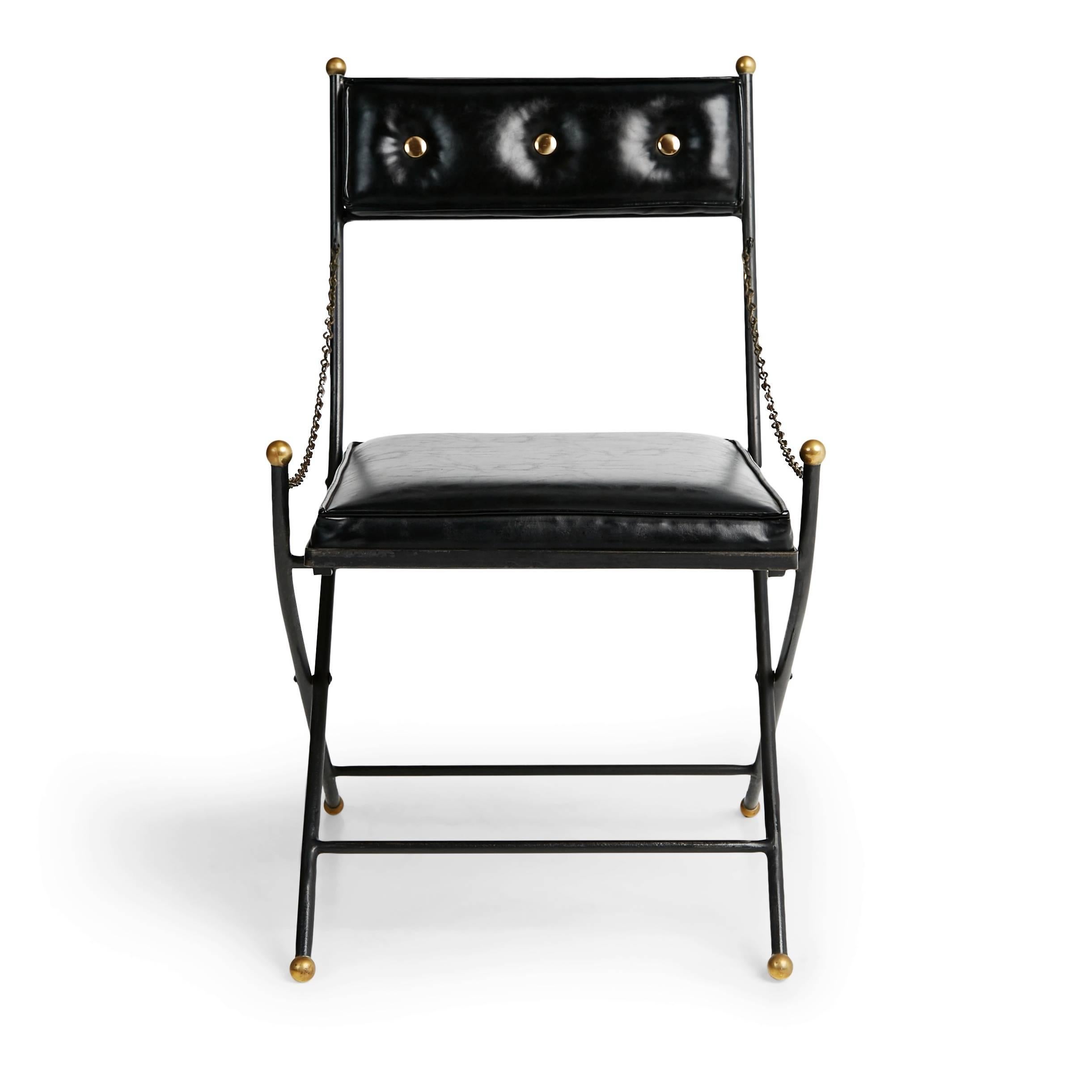 Set of eight Campaign folding chairs in the style of Maison Jansen and Tommi Parzinger. This elegant Mid-Century Modern set comprises of four red and four black folding chairs upholstered in faux leather. They feature brass metal embellishments on