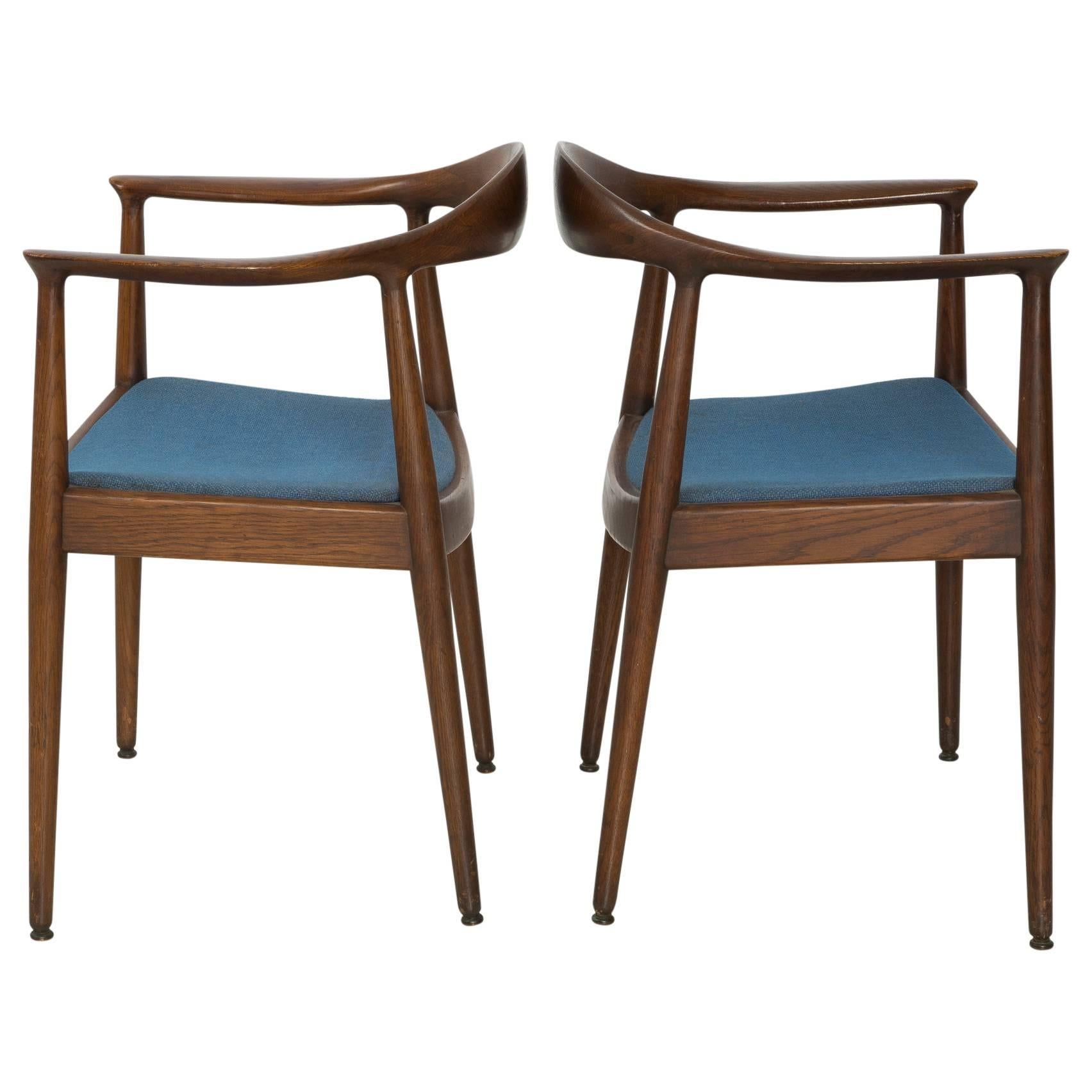 A sculpted pair of Danish Modern arm chairs, attributed to "The Chair" by Hans Wegner, circa 1960. The sinuous lines the rounded oak back rest glide into arm rests. The dark oak frames are a beautiful contrast to the bold, blue upholstery.