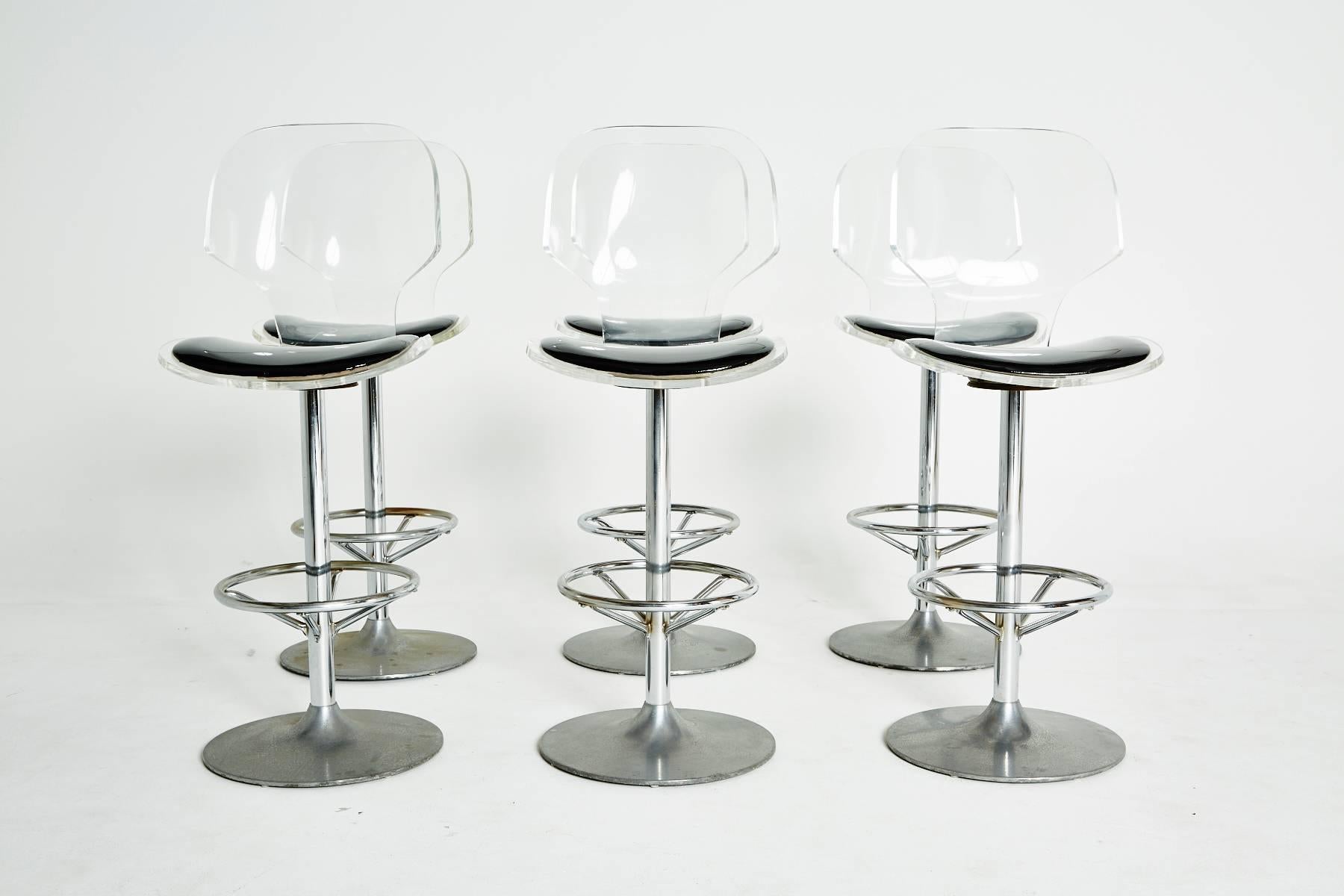 This set of six (6) classic mid-century lucite bar stools by Hill Manufacturing with curved Lucite clamshell backrests and seats adorned by black glossed cushions. The swiveling seats are mounted on chrome bases with circular footrests. 

Lucite
