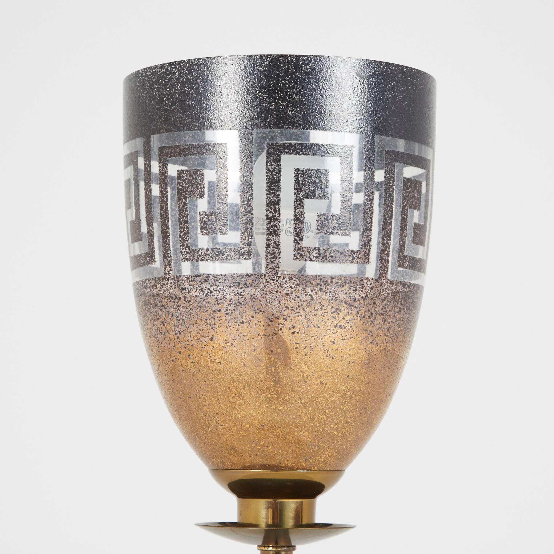 Founded in Chicago in 1932, Stiffel has remained an industry leader and innovator for over seven decades. A tapering glass shade is decorated with a black and gold Greek key design. The lamp's brass sconce is placed atop a slender stem and square