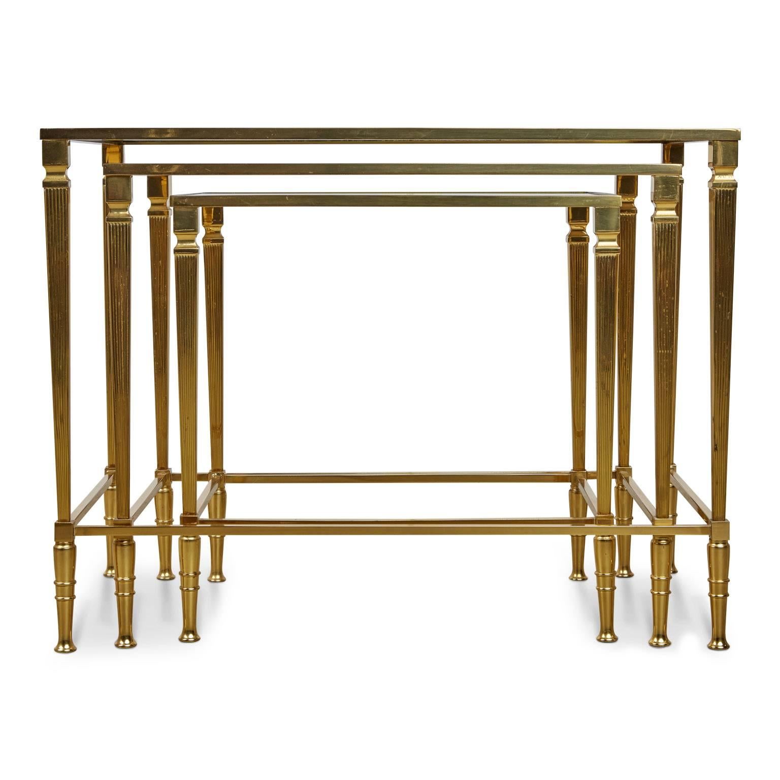 Set of three Regency style polished Italian nesting tables. Fabricated from gleaming polished brass with slender reeded legs and glass tops with contrast mirror edge borders on each. These compact side tables fit neatly in to one another to conserve