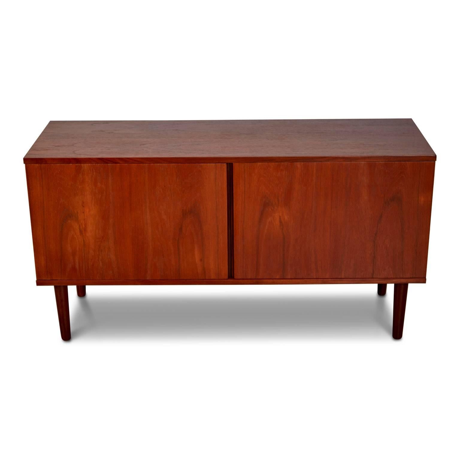 Petitely proportioned Scandinavian credenza fabricated from teak. The slender, simplistic design comprises of two doors which open to reveal shelf spaces either side - perfect for storing dish ware, table linens and other household items and is set