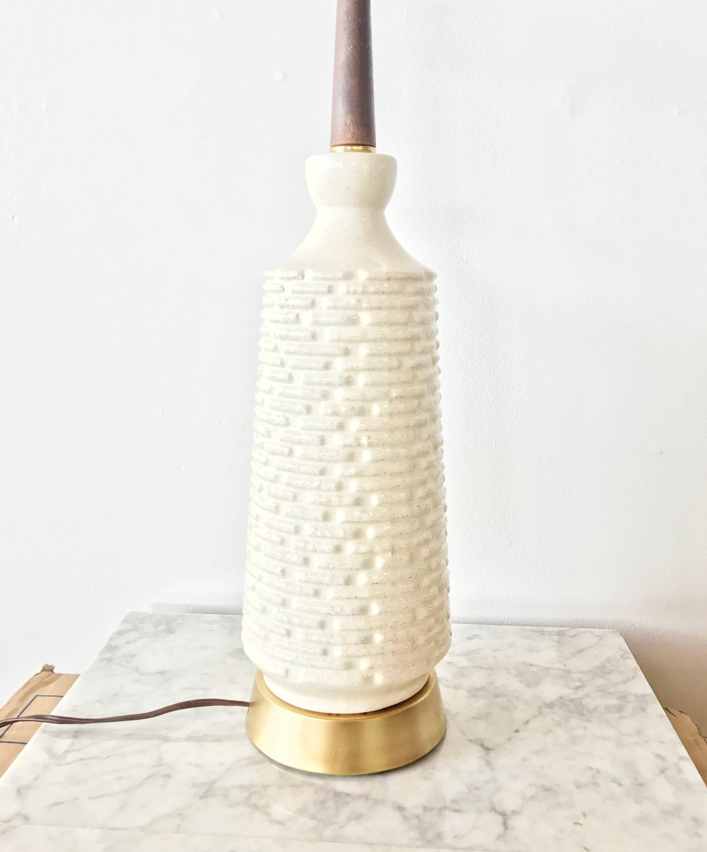 Wonderfully textured ceramic lamp, circa 1960. Featuring a subtly moulded geometric grid pattern that progresses across the body of the lamp which is affixed to a gold toned base with a wooden neck. 

This table lamp can be used in a dining room,