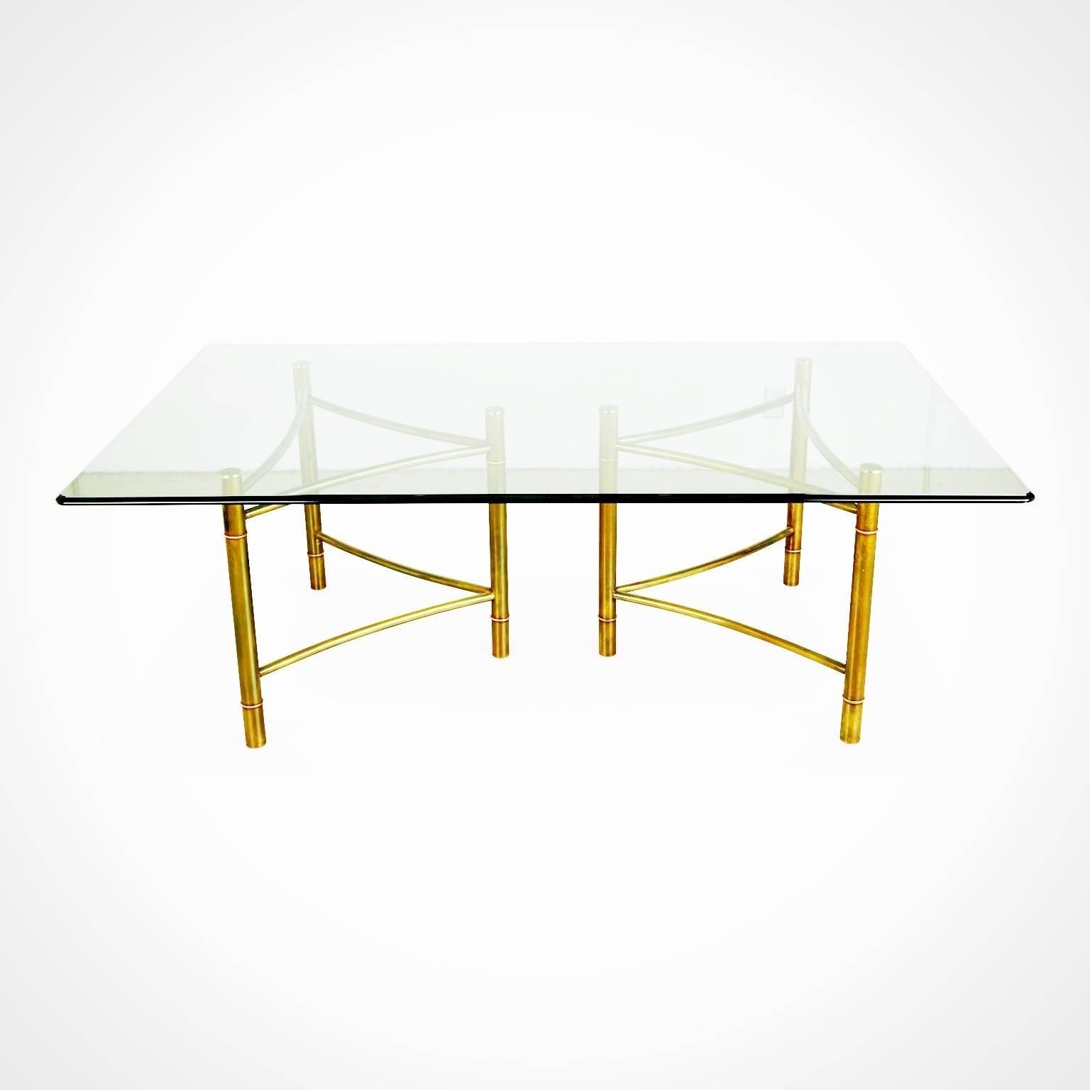 Gleaming brass Mastercraft dining table with expansive rectangular glass top with beveled edge. The rectangular bases each feature three sturdy posts which are connected by gracefully curved stretchers. The contrast between the straight vertical