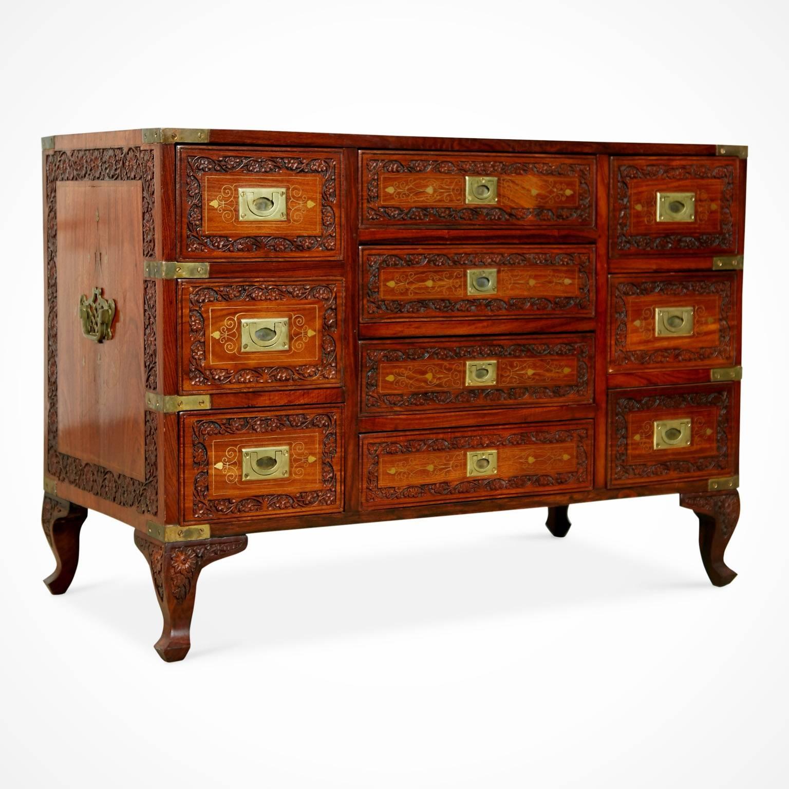 Intricately carved inlay Campaign dresser or chest with ten drawers. Fabricated from walnut which has an intrinsically carved floral border detail around the top, sides, cabriole legs and each individual drawer. This dresser features gleaming brass