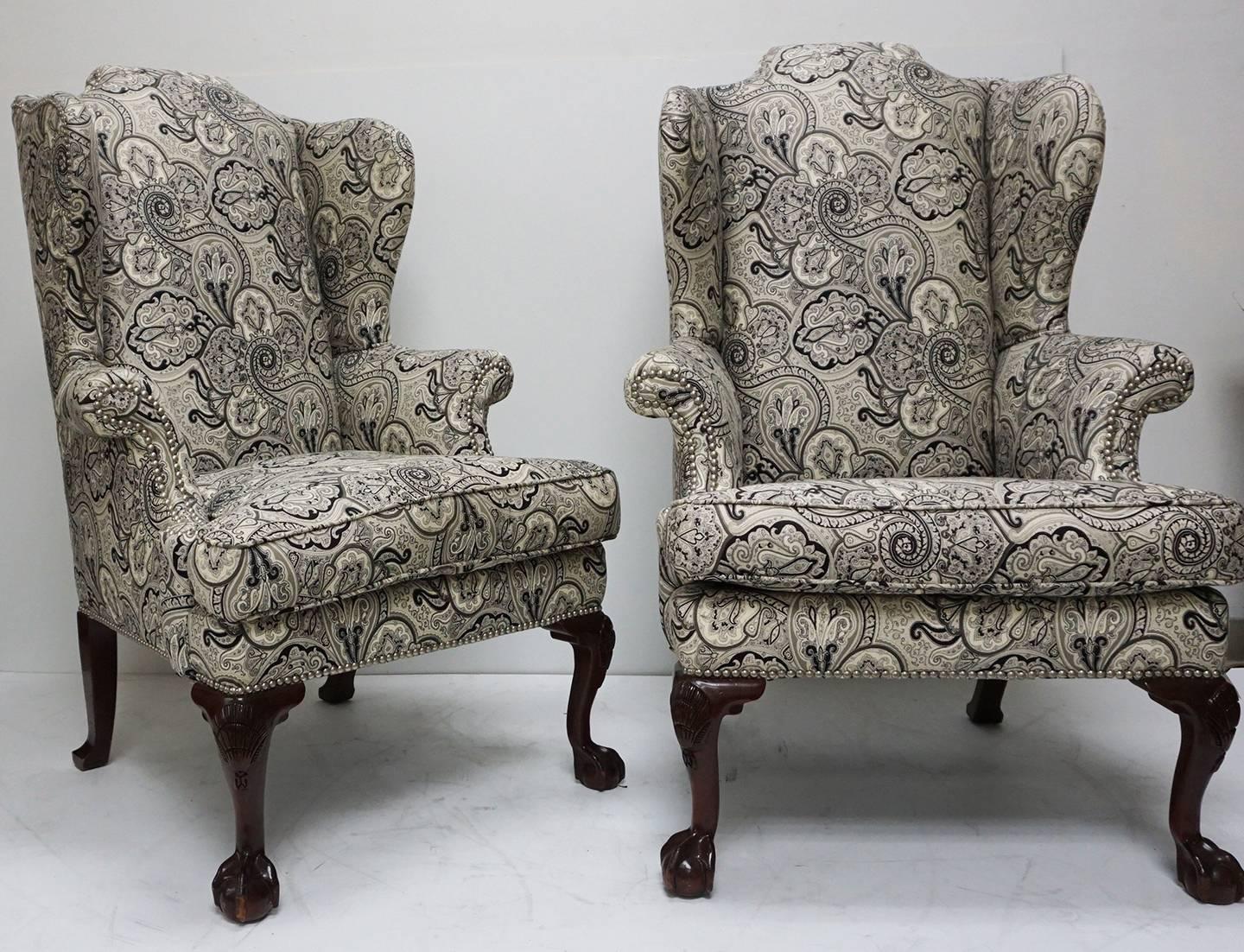 A pair of wing chairs updated with a black, grey and off-white paisley upholstery and accented with chrome tacks. Ball and claw mahogany legs in the manner of George II.