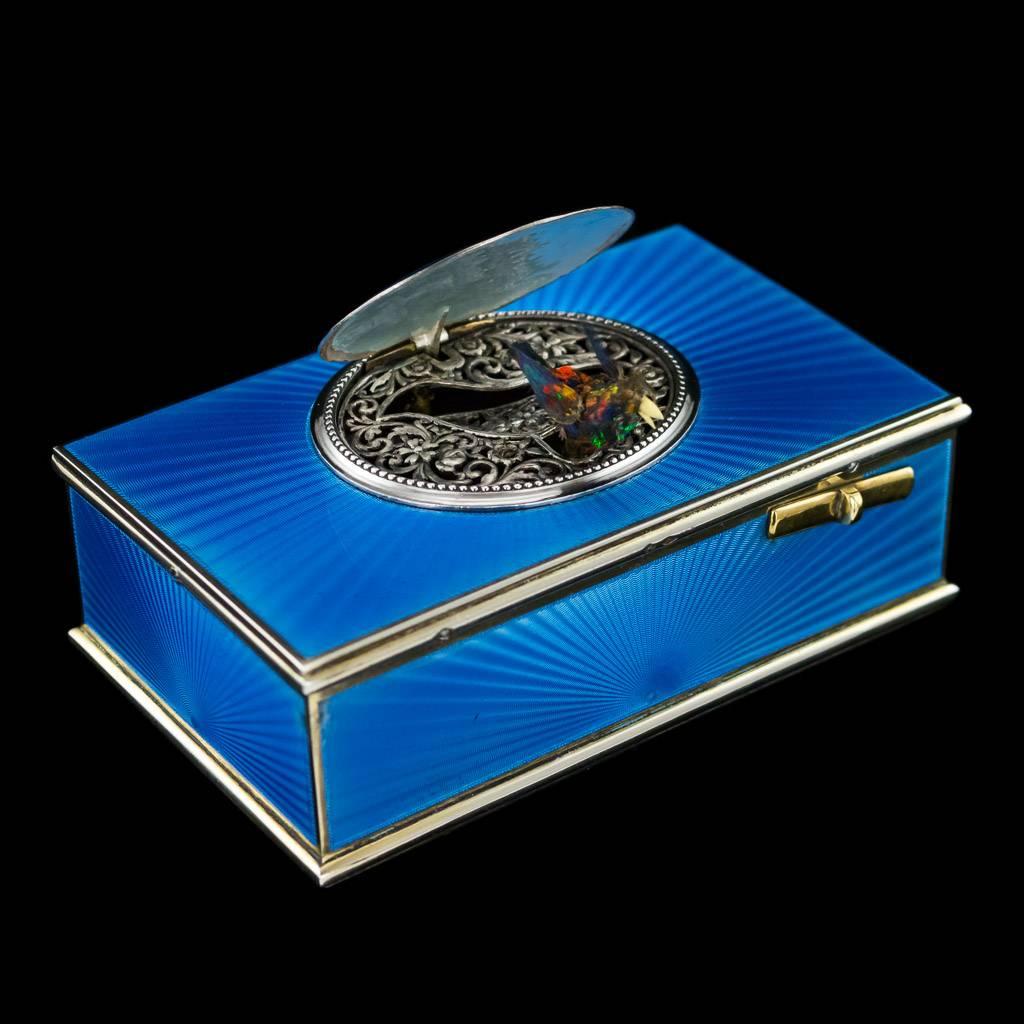 Antique early-20th century rare French solid silver-gilt singing bird automaton box, of rectangular form, guilloche enamelled in translucent blue over a sun ray and wavy engine-turned ground, the oval cover enamelled with views of the countryside at