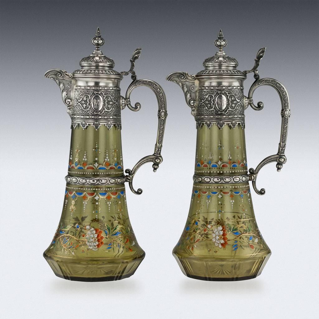 DESCRIPTION

Antique 19th Century German solid silver & enameled glass pair of large and decorative wine claret jugs, each baluster form glass body beautifully enameled with multi-colour foliate scroll decoration, mounted with a silver collar chased