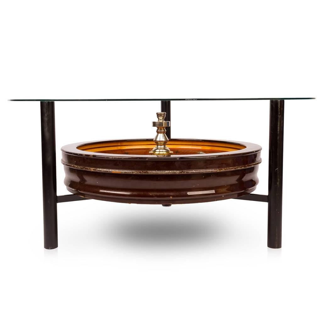 A particularly rare and stylish 20th century novelty roulette wheel coffee table, the polished veneered wood wheel with working spinning centre made by John Huxley of London, set on a three feet support and with round glass top.

The table is