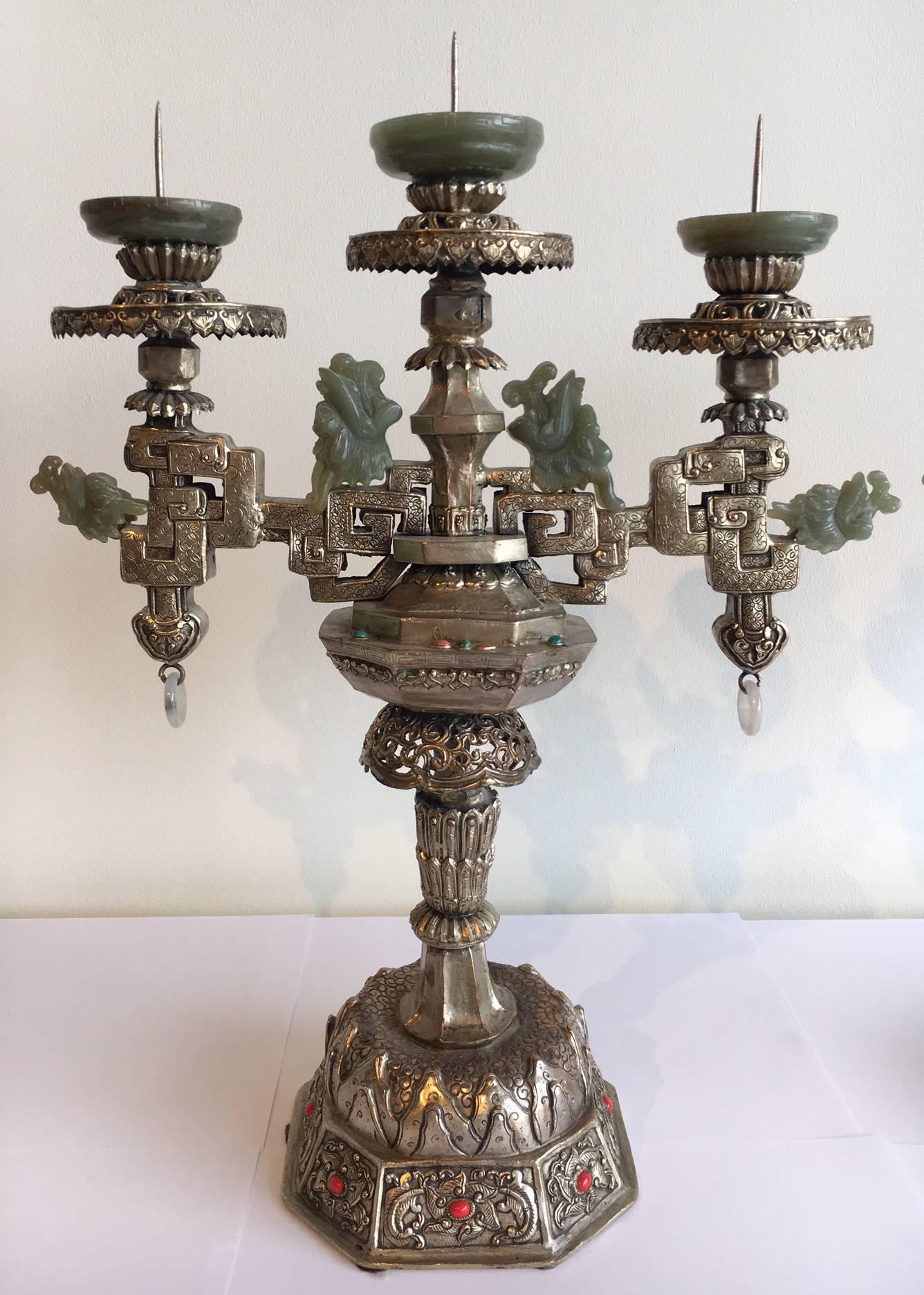 This candelabra is made of silver, and adorned in semi-precious stones. 
It is inlaid with turquoise, coral, and bowenite. It's Mongolian in style, and features intricate carvings made of jade. 
Made in the late 20th century.

We currently have two