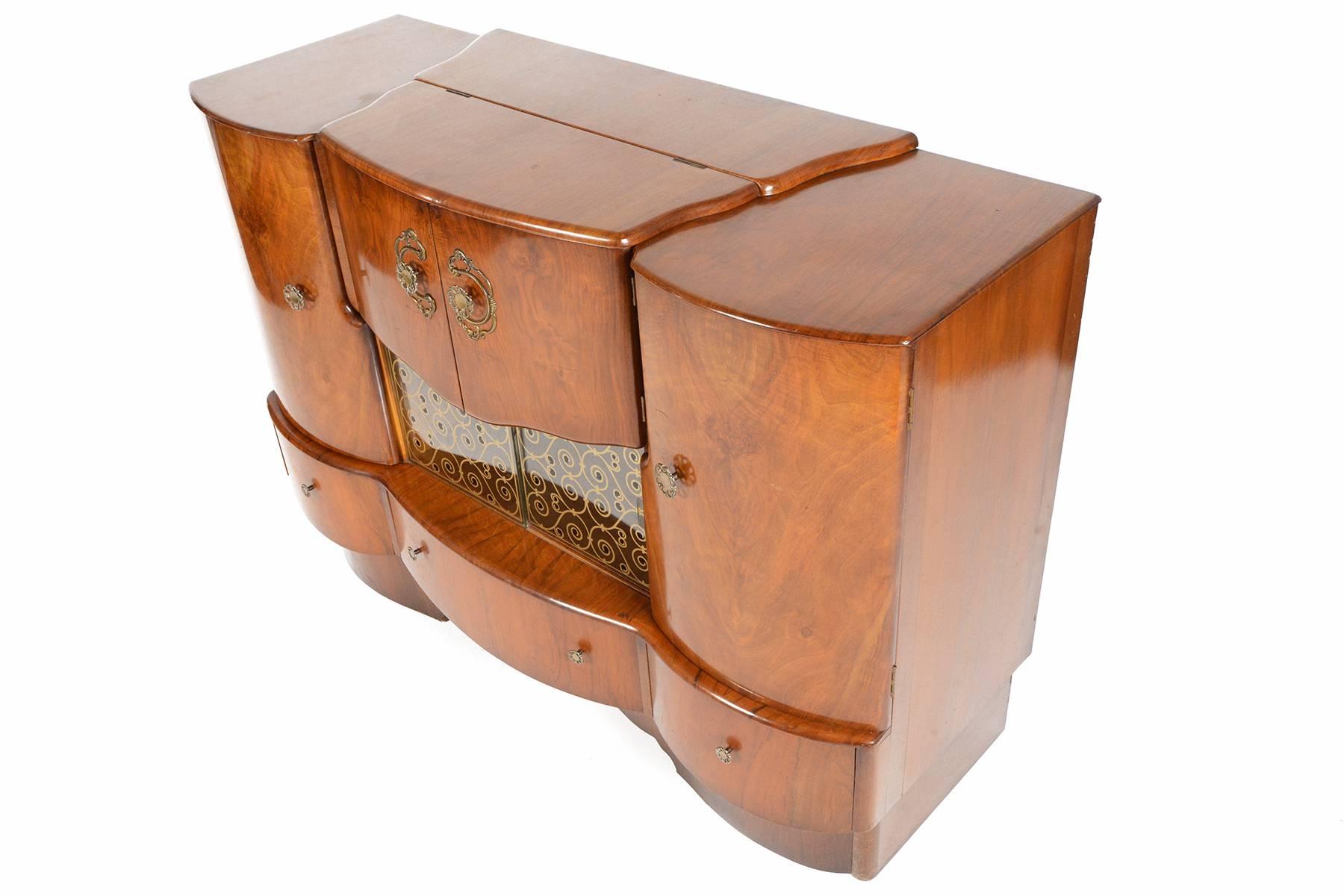 This stunning English modern bar in elm is a staple of a bygone era! The gorgeous elmwood case was crafted in the early 1940s and offers the soft lines popular during the Art Deco period. Left and right cabinet doors are adorned with their original
