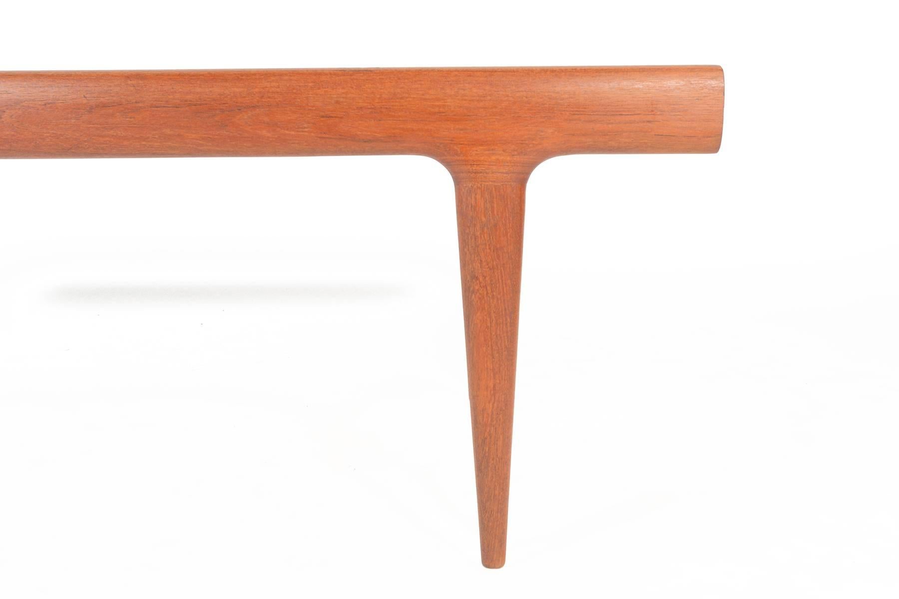 This Danish Modern Mid-Century coffee table in teak was designed by Johannes Andersen for Uldum Møbelfabrik in the 1960s. Expertly built, this gorgeous piece features solid teak legs which are seamlessly joined to the tabletop. A pull-out storage