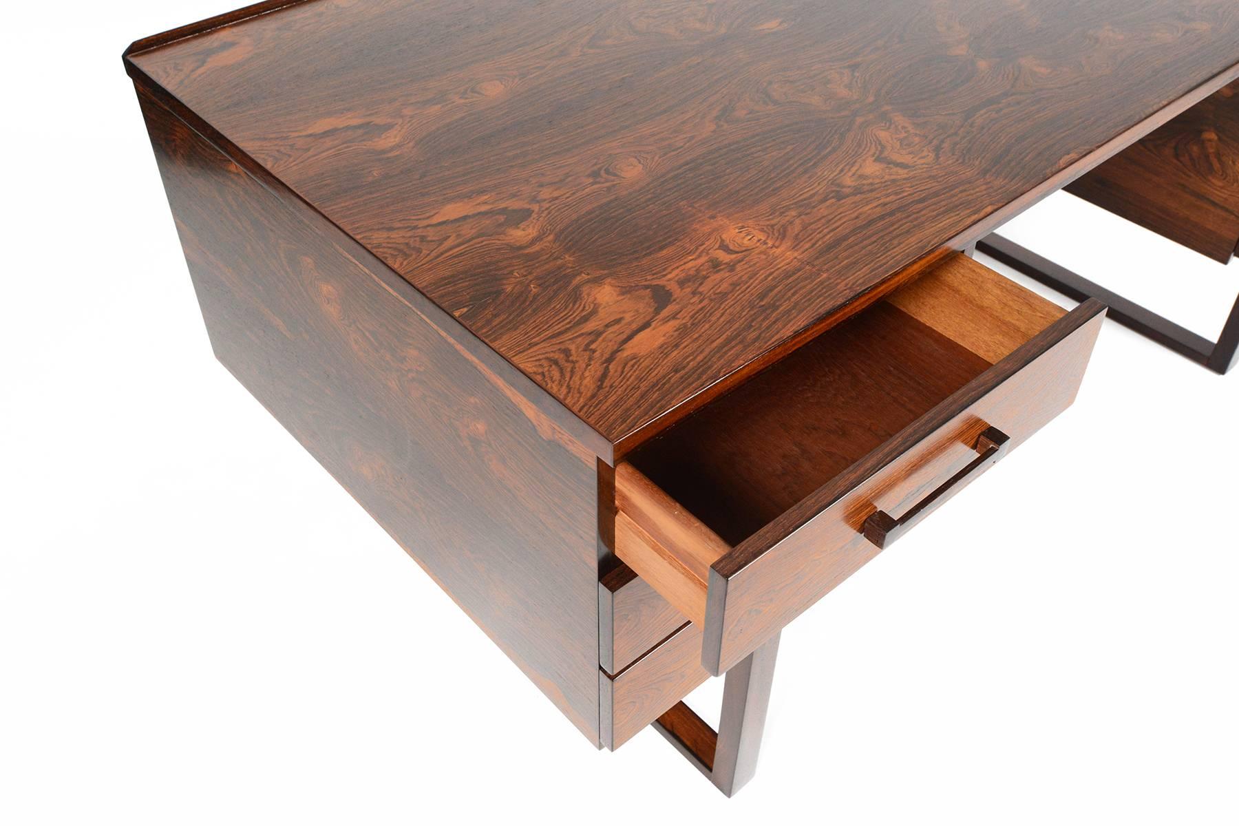This rare Danish modern executive desk was designed by Henning Jensen and Torben Valeur in the 1960s. Crafted in Brazilian rosewood, the top slab features vivid cathedral grain patterns. The spacious kneehole is nestled between two banks of drawers.