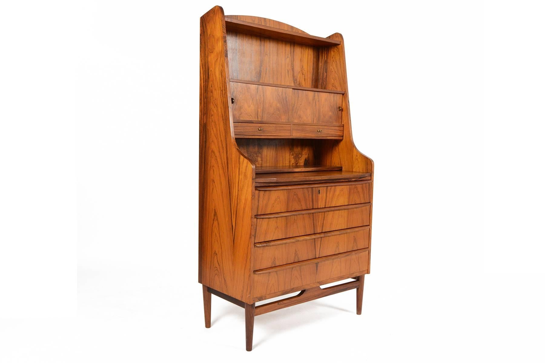 This Danish modern Mid-Century secretary desk is fantastically preserved. Crafted in Brazilian rosewood, this gorgeous piece features a pullout desk surface. A cubby is concealed with two doors with brass crescent pulls. Four large lower drawers