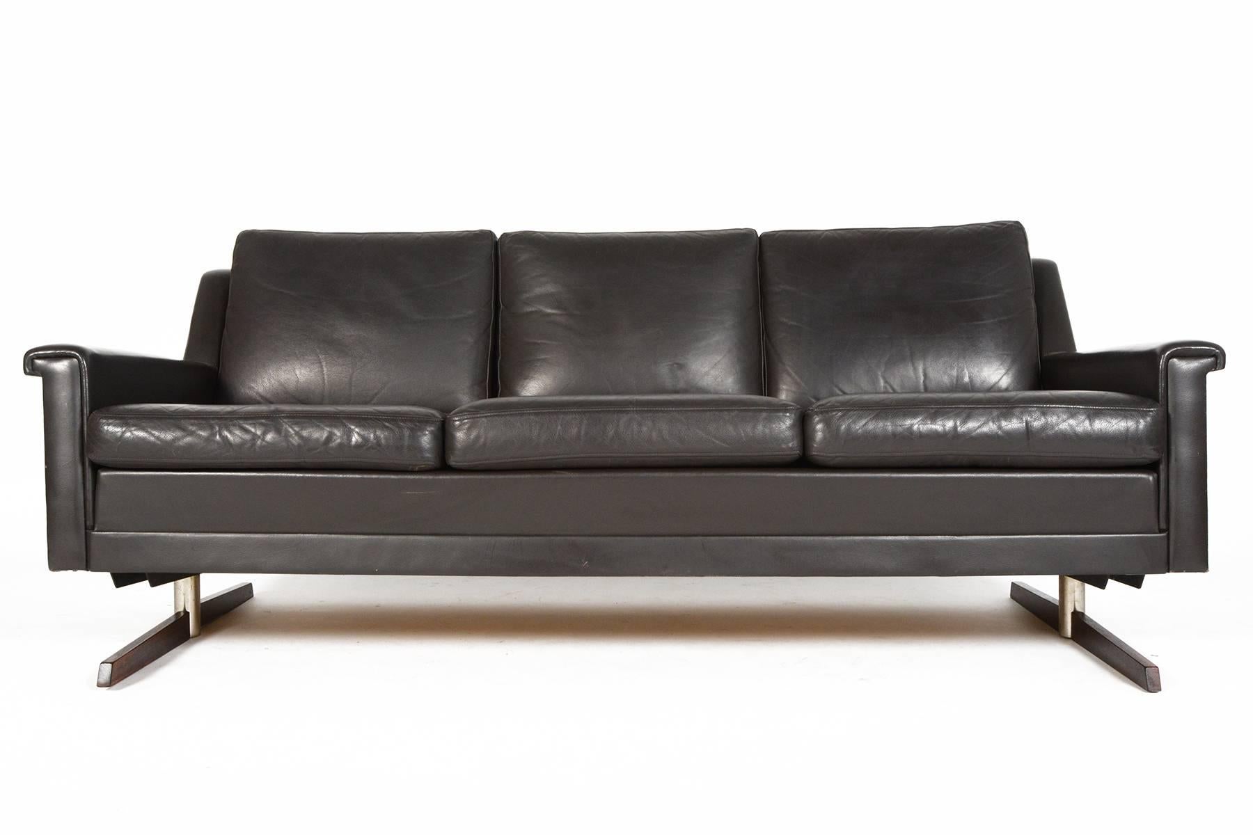 This Danish modern Mid-Century three-seat sofa in chocolate leather offers a Classic Silhouette with an early 1970s modern steel and rosewood base. Cushions wear their original patinated deep chocolate leather upholstery. Finished on all sides, this
