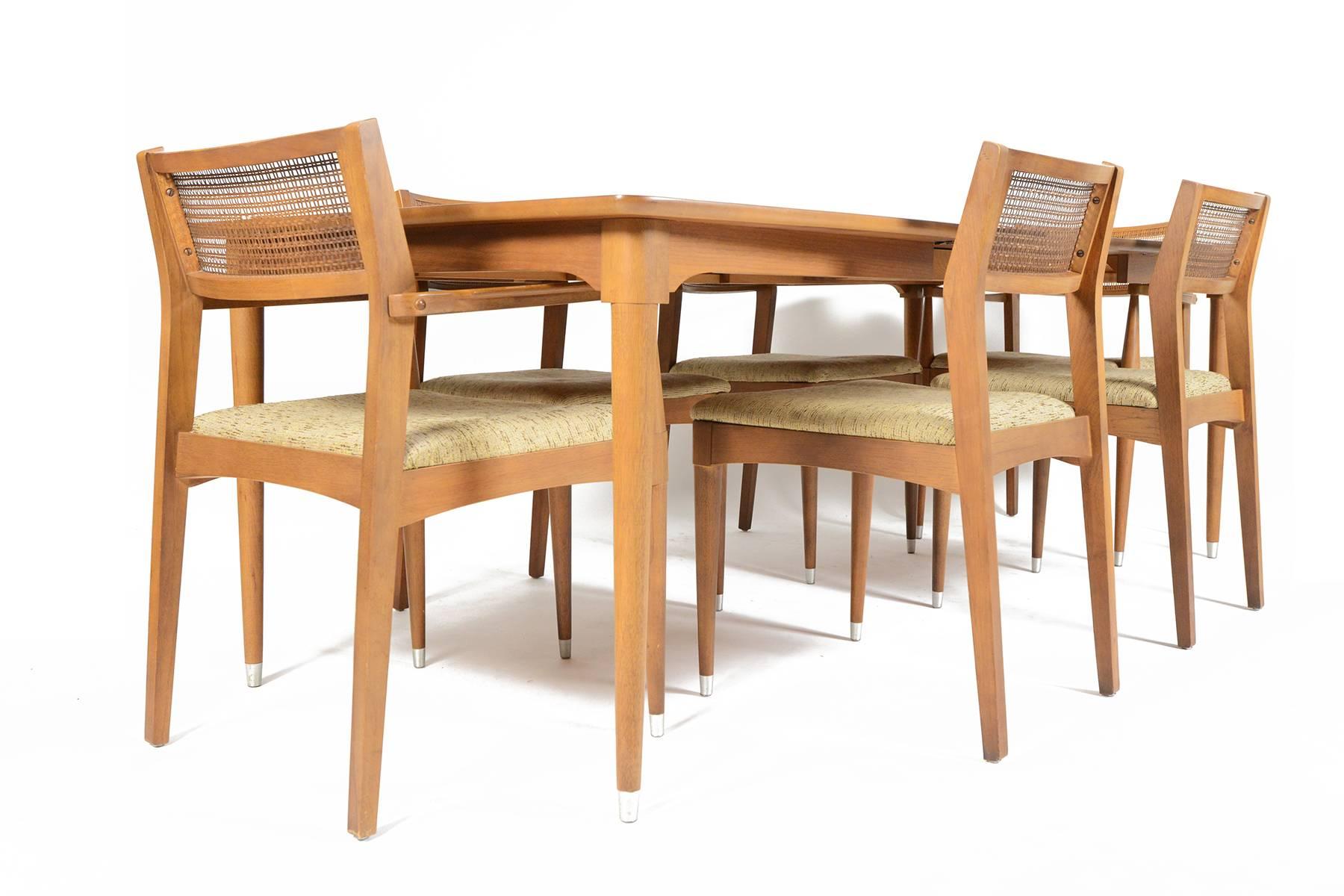 Wonderfully preserved, this stately B.P. John American Mid-Century Correlaire Collection dining set in walnut is a fantastic set for any dining room. The set of six chairs includes two captains chairs. Original cane backrests create an airy, open