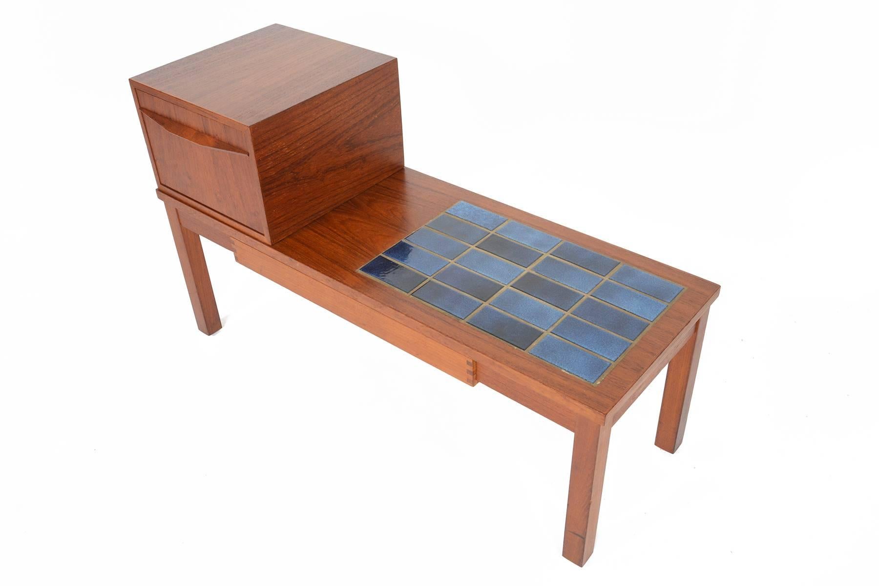 This Danish Mid-Century Modern telephone bench is crafted in teak and rests on sculpted legs. Perfect for any entryway, this time capsule piece features blue tiles! In excellent original condition with typical wear for its vintage.