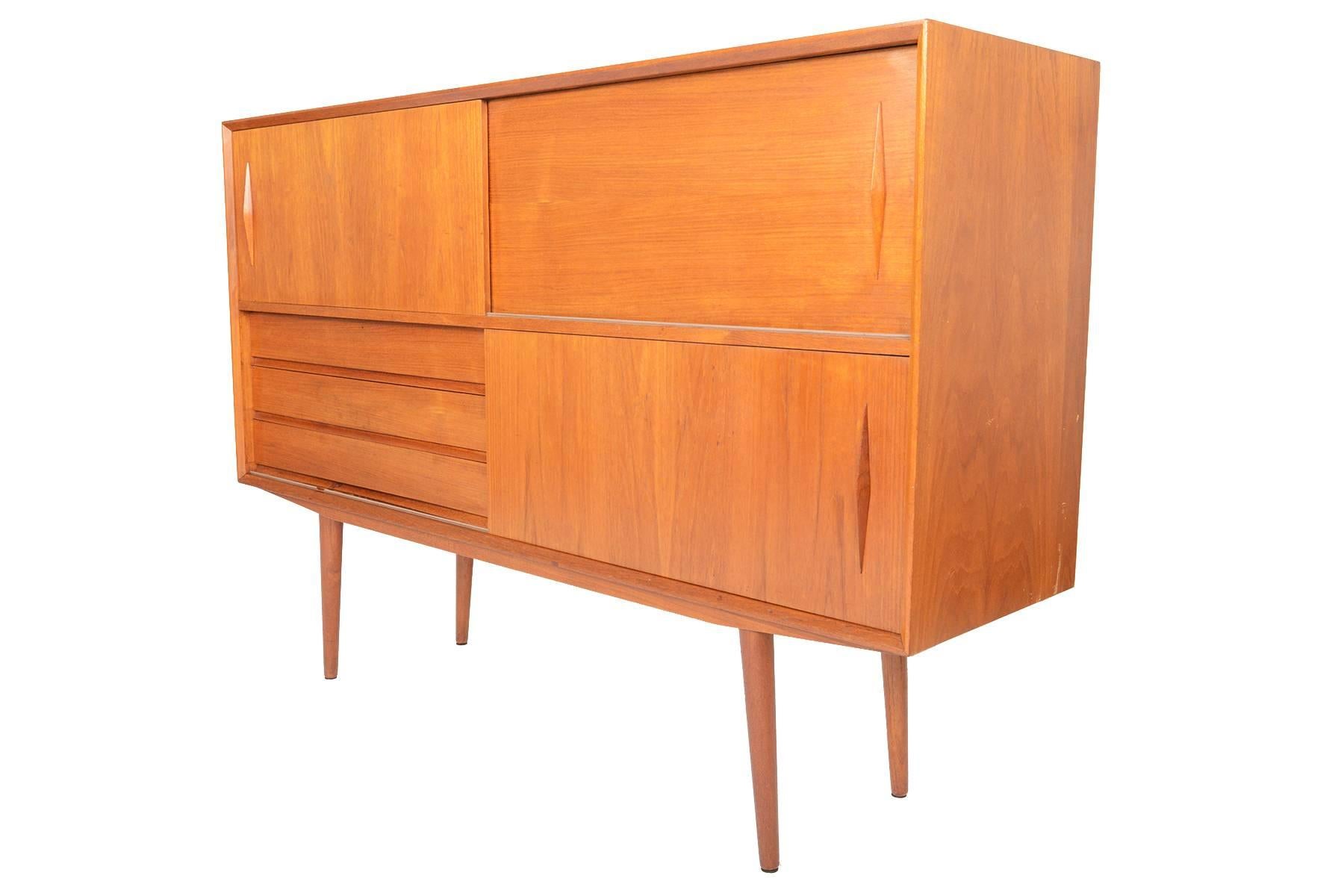 This beautiful streamline tall teak credenza is a wonderful case piece with excellent storage capabilities! Two sliding doors sit at the top of this piece adorned with diamond carved teak pulls. Doors open to reveal two bays, each with an adjustable
