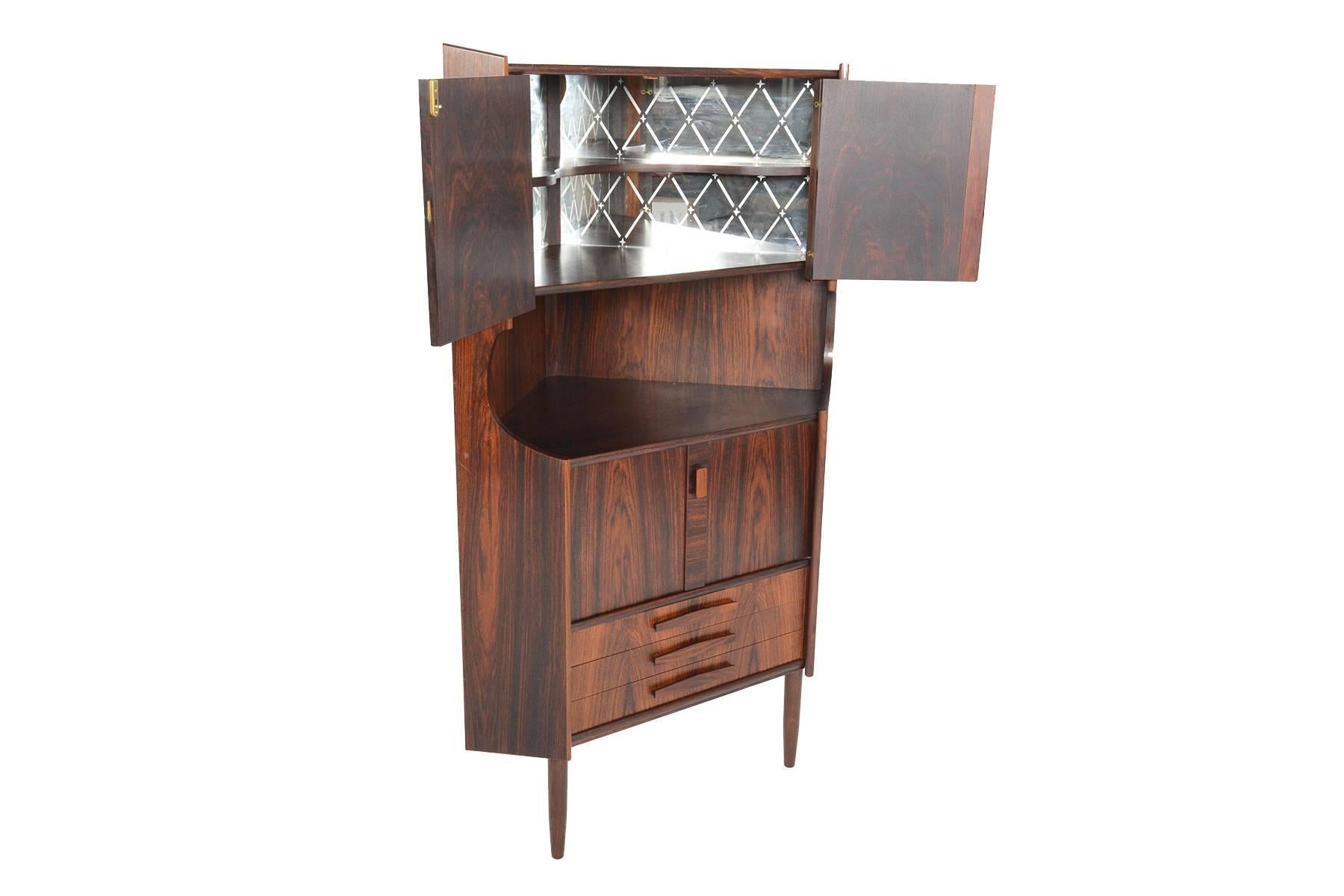 This Danish modern Mid-Century corner cabinet is the perfect storage solution for any home. This tall corner unit offers a bar outfitted with an etched glass backing. A lower cubby, cabinet, and three drawers complete this piece. In excellent
