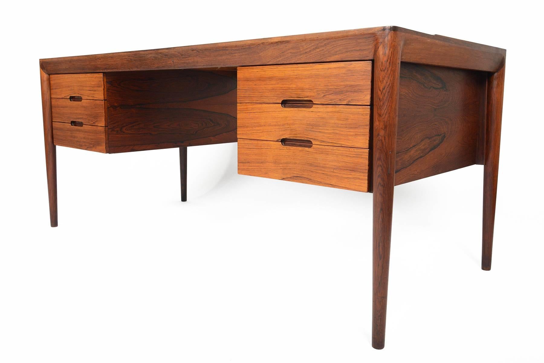 This rare Danish modern executive desk was designed by Erik Riisager Hansen for Haslev Møbelsnedkeri in the 1960s. The beautiful thick banding seamless joins with the tall spindle leg and is a signature design element of the Hansen. Crafted in