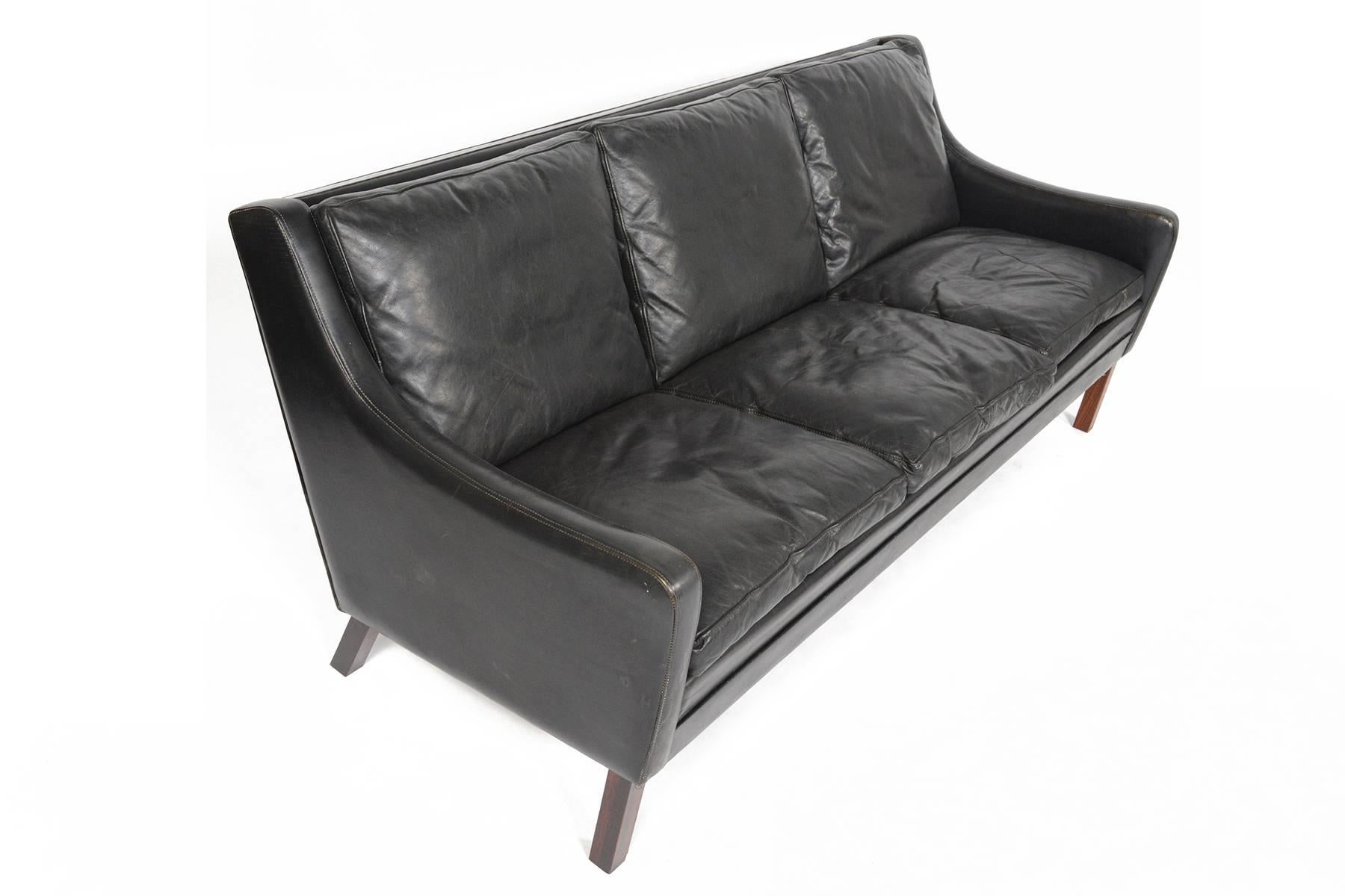 This Danish modern Mid-Century three seat sofa in black patinated leather is a staple of modern decor. This completely original sofa is covered in buttery soft leather and filled with down for an extra comfortable seating experience. Gorgeous