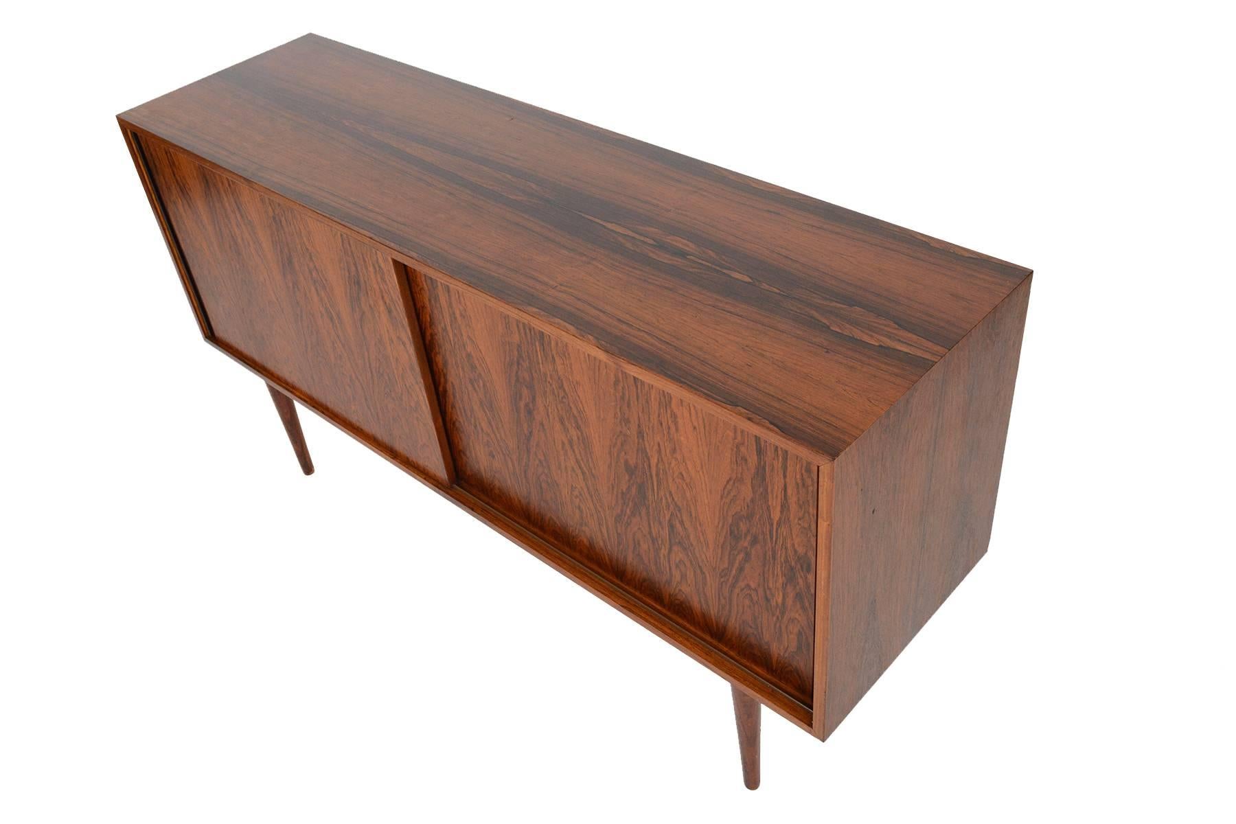 This Danish modern Mid-Century credenza hails from the 1960s and is perfectly sized for any modern living space. Crafted in Brazilian rosewood with handsomely refined lines, two sliding doors open to reveal two bays with adjustable shelving. In