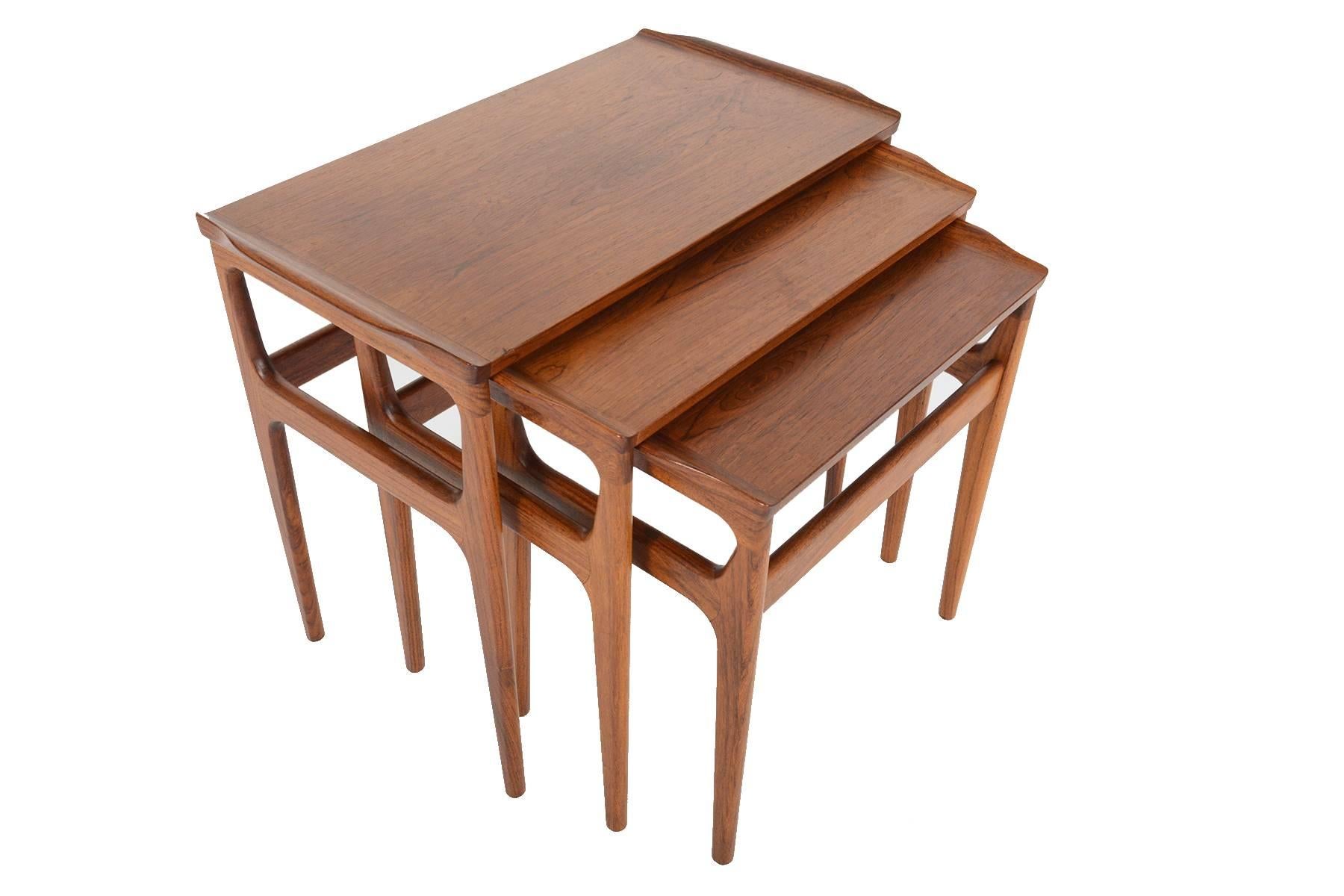 This wonderful set of Danish modern Mid-Century nesting tables in Brazilian rosewood by Heltborg Mobler are extremely versatile. Table tops feature a delicate raised lip on either end for convenient handling. Beautifully tapered long rosewood legs