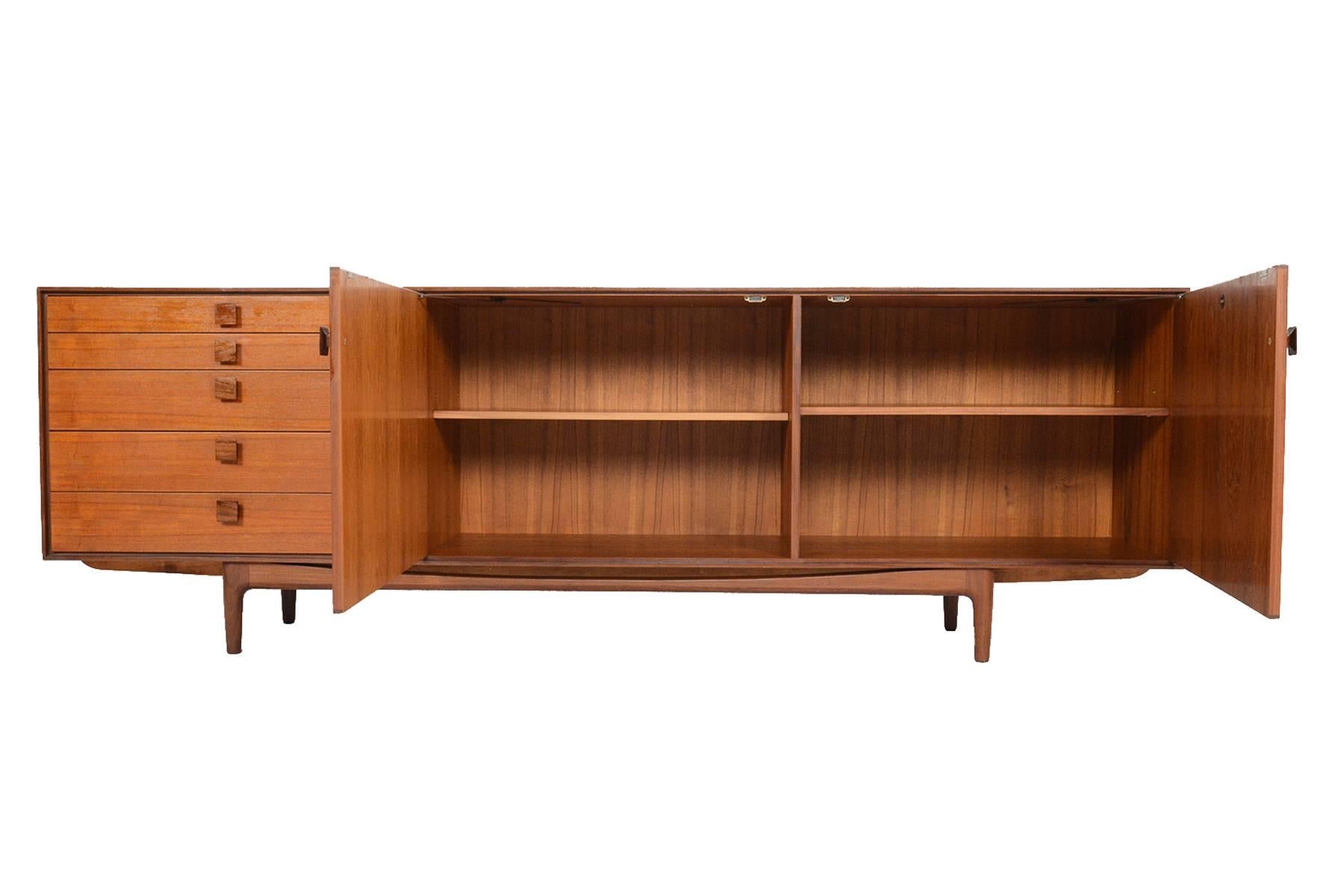 This Danish modern Mid-Century large teak credenza was designed by Ib Kofod- Larsen for Grange and Branches in the 1960s. Crafted in teak with handsomely refined lines, five drawers with the designer's signature carved teak pulls sit on the left of