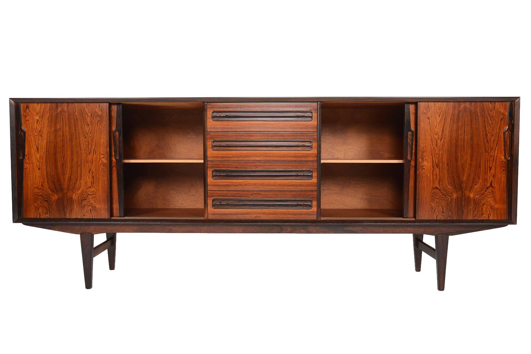 This large Danish modern rosewood credenza was designed by Ærthøj Jensen & Mølholm in the 1960s. Stunning wood grain is showcased on the sliding doors and case. Contrasting drawer pulls and banding highlight the exceptional grain patterns