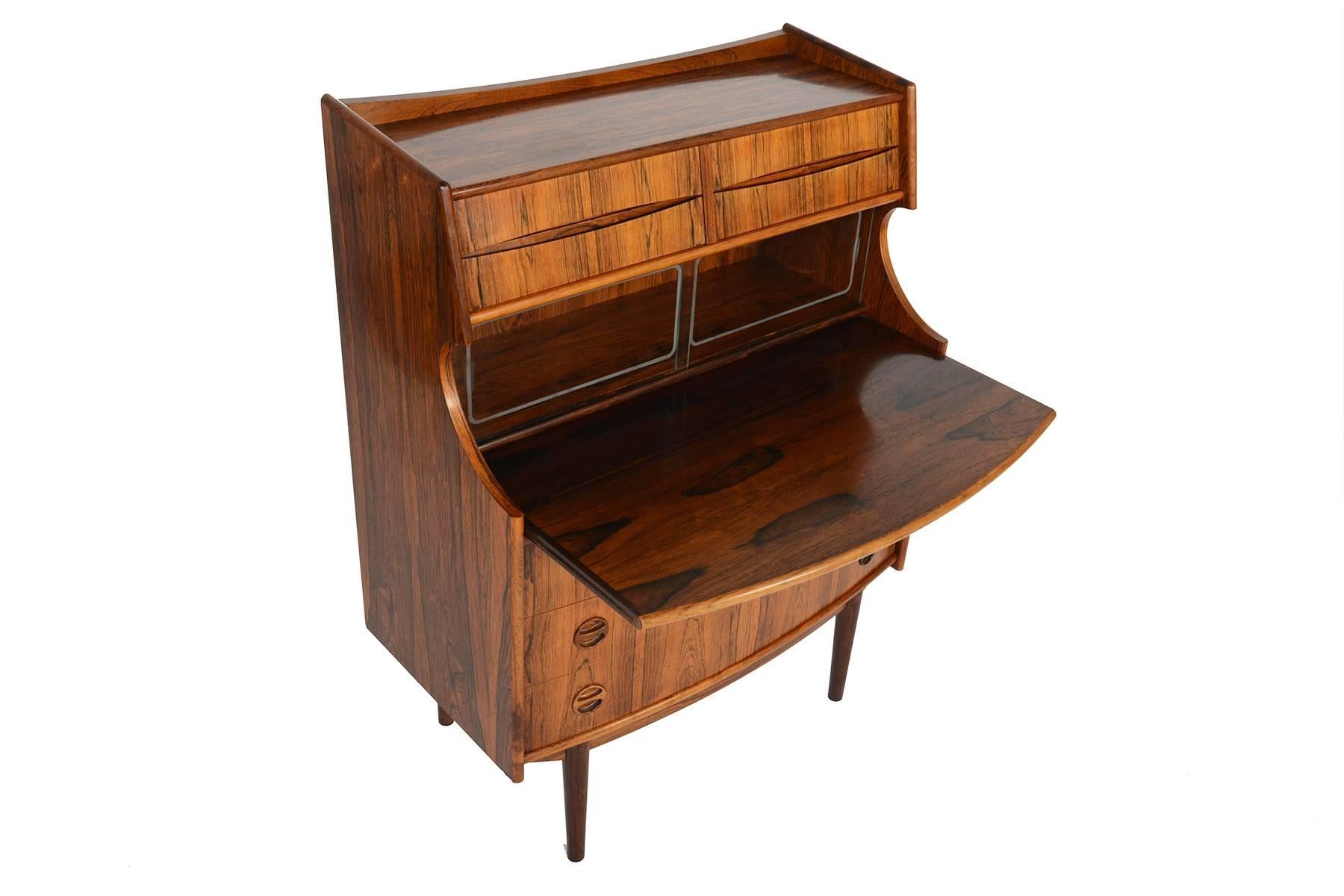 This incredible Danish modern secretary desk by Falsigs Møbelfabrik in rosewood hails straight from the 1960s! The centre of this piece features a pullout desk and provides a spacious work surface. Two etched glass doors sit above. Four small upper