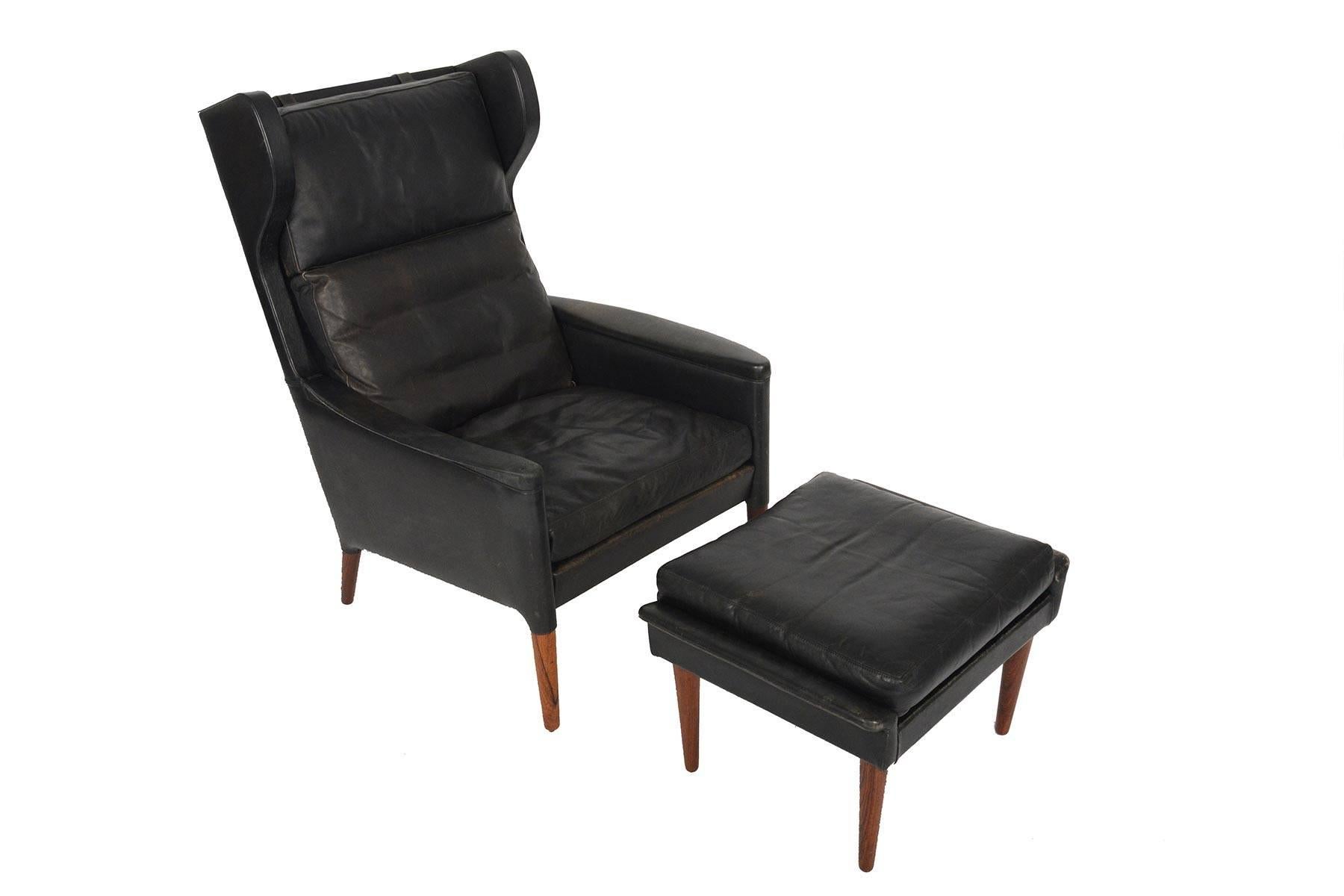 This Danish modern black leather wingback lounge chair and matching ottoman were designed by Kurt Østervig for Centrum Møbler as Model 55 in 1965. Beautifully crafted with solid Brazilian rosewood spindle legs, this set offers design details unlike