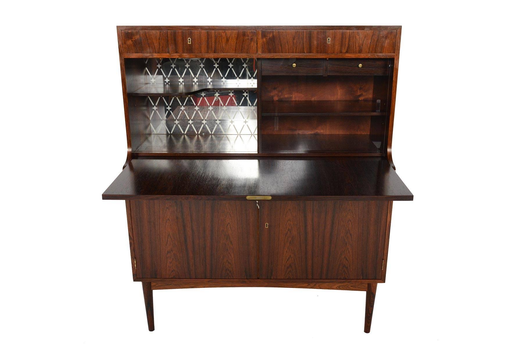 This astounding Danish modern secretary desk in rosewood is a jack of all trades! The centre of this piece features a pullout desk and provides a spacious work surface. Once the door is lowered, a beautiful etched mirror bar with shelving sits to