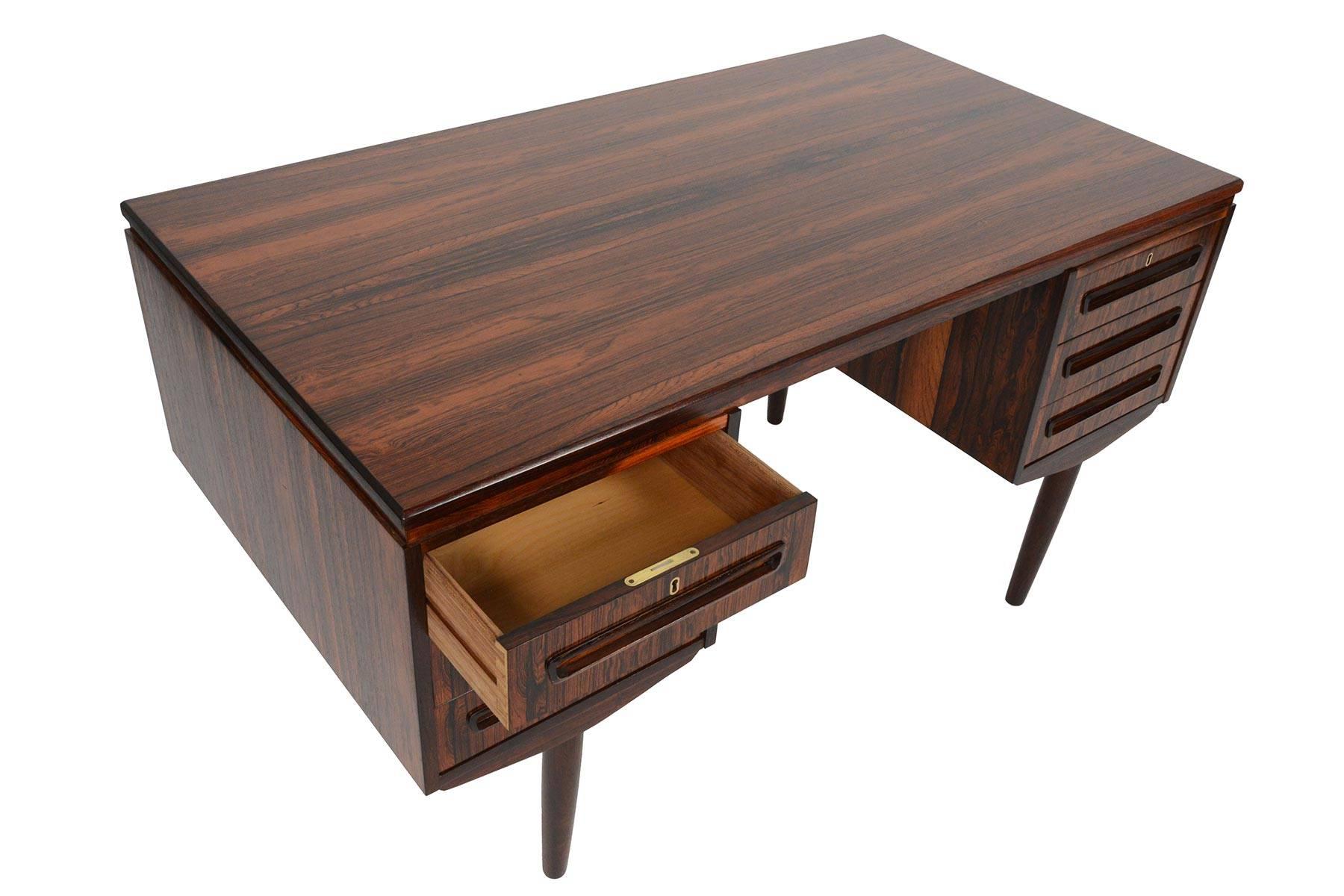 This Danish modern desk in Brazilian rosewood is a wonderfully piece for any home or office. The top of this desk features a beautiful slab of rosewood with active cathedral grain patterns. Two banks of three drawers sit on either side of the