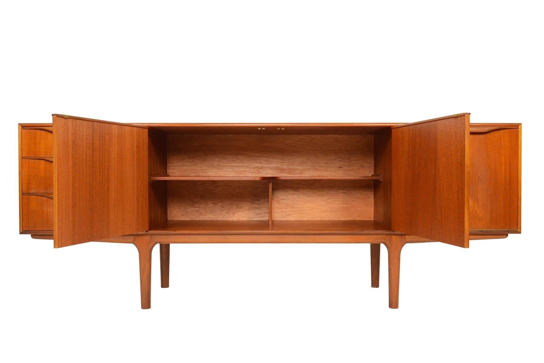 This Mid-Century Modern large low line teak sideboard by A.H. McIntosh is from the Dunvegan Range. Two center doors open to reveal a fixed asymmetrical bar shelf. Right bar cabinet drops down to reveal open storage, and a slide out laminated drink