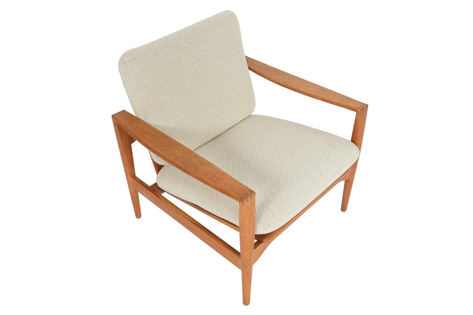 This Danish modern lounge chair known as the EK model, was designed by Illum Wikkelsø for Niels Eilersen in the 1960s. Gorgeous sculpted quarter- sawn oak arms with distinctive finger joinery add a unique touch to this spectacular piece. Recently