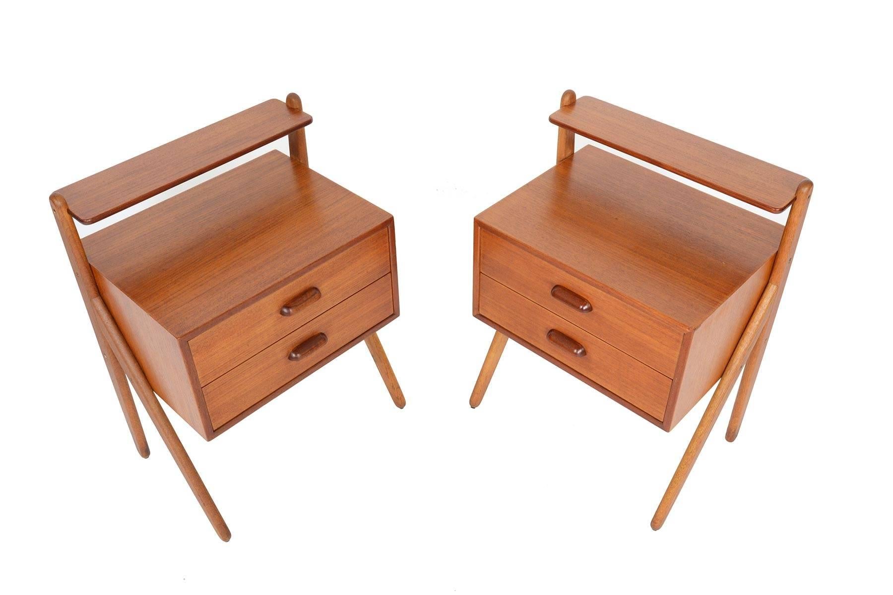 This lovely pair of Danish modern midcentury V-legged nightstands were manufactured by Ølholm Møbelfabrik. Crafted in teak with gorgeous oak legs, these nightstands offer two drawers and a small shelf. In excellent original condition with typical