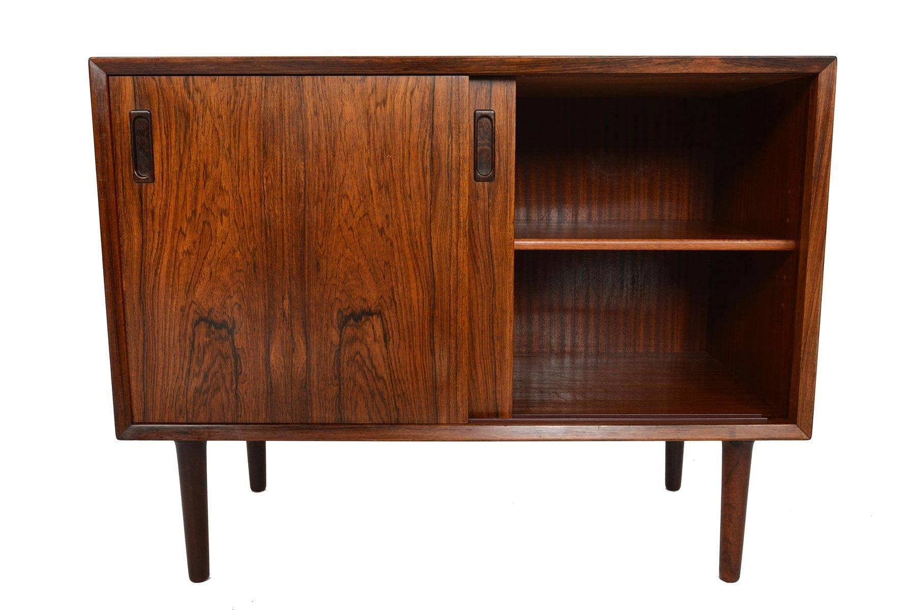 This small Danish modern midcentury credenza by Lyby Møbler is a perfect storage solution for any modern home. Crafted in brilliantly grained rosewood, two sliding doors with carved rectangle shaped pulls open to an adjustable shelf. In excellent