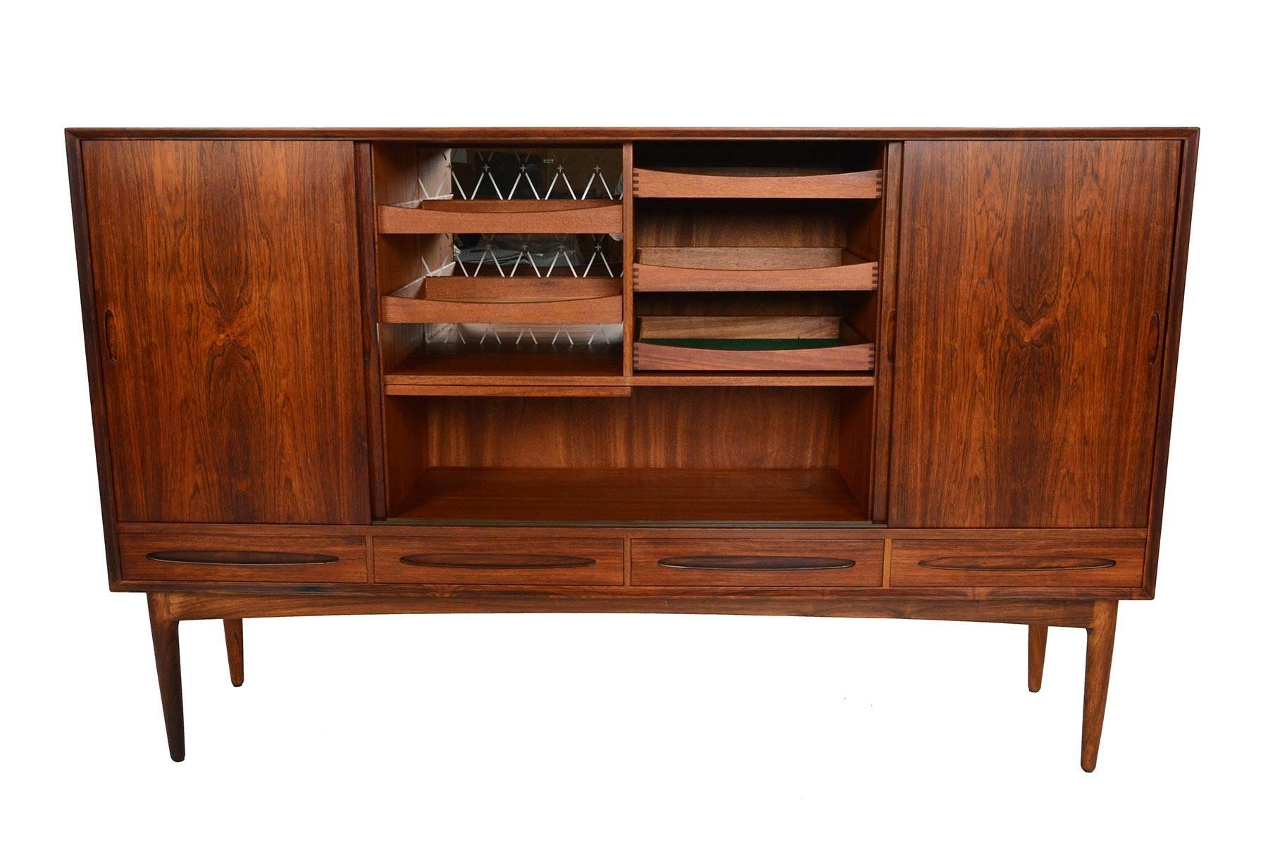 This tall Danish modern midcentury credenza is crafted in Brazilian rosewood and showcases gorgeous active grain patterning throughout. Four large doors slide open to reveal three bays. The left and right bays house six adjustable shelves while the
