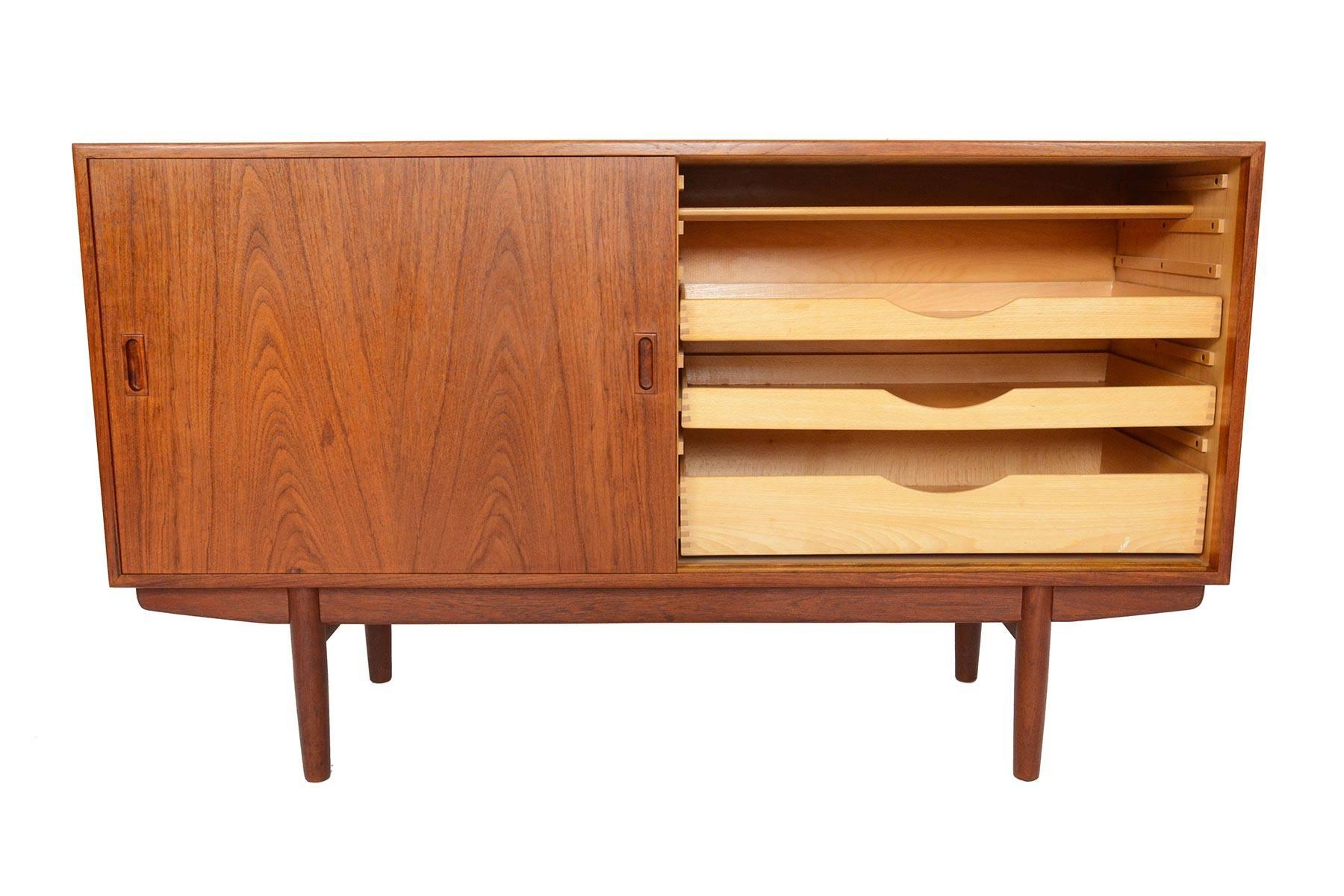 This Danish modern sliding door credenza in teak was designed by Børge Mogensen for Søborg Møbelfabrik. Designed in 1953, this piece features the designer's signature base and solid joinery. Two doors slide open to reveal three adjustable shelves