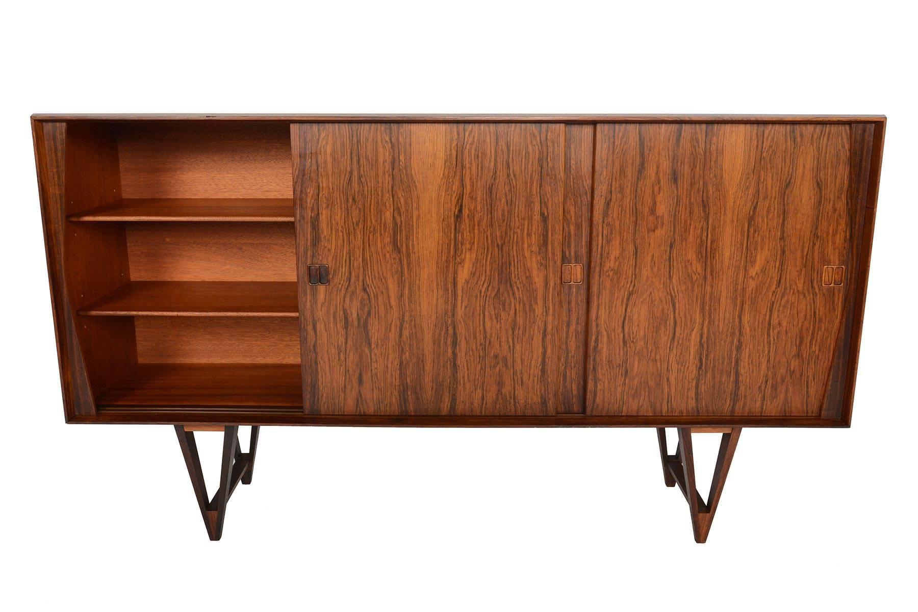 This fantastic Danish modern tall credenza is crafted from rosewood and its large case virtually floats with its astounding v- leg base! Three sliding doors reveal two large bays with adjustable shelving on either side of a centrally located bar. An