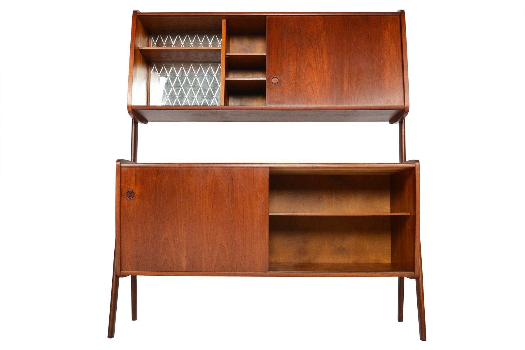 This wonderful Danish modern teak credenza with hutch offers two tiers of storage with a wonderfully airy design! The top hutch features a mirror lined bar and an open storage bay with two adjustable shelves. Beautiful exterior legs form the brace