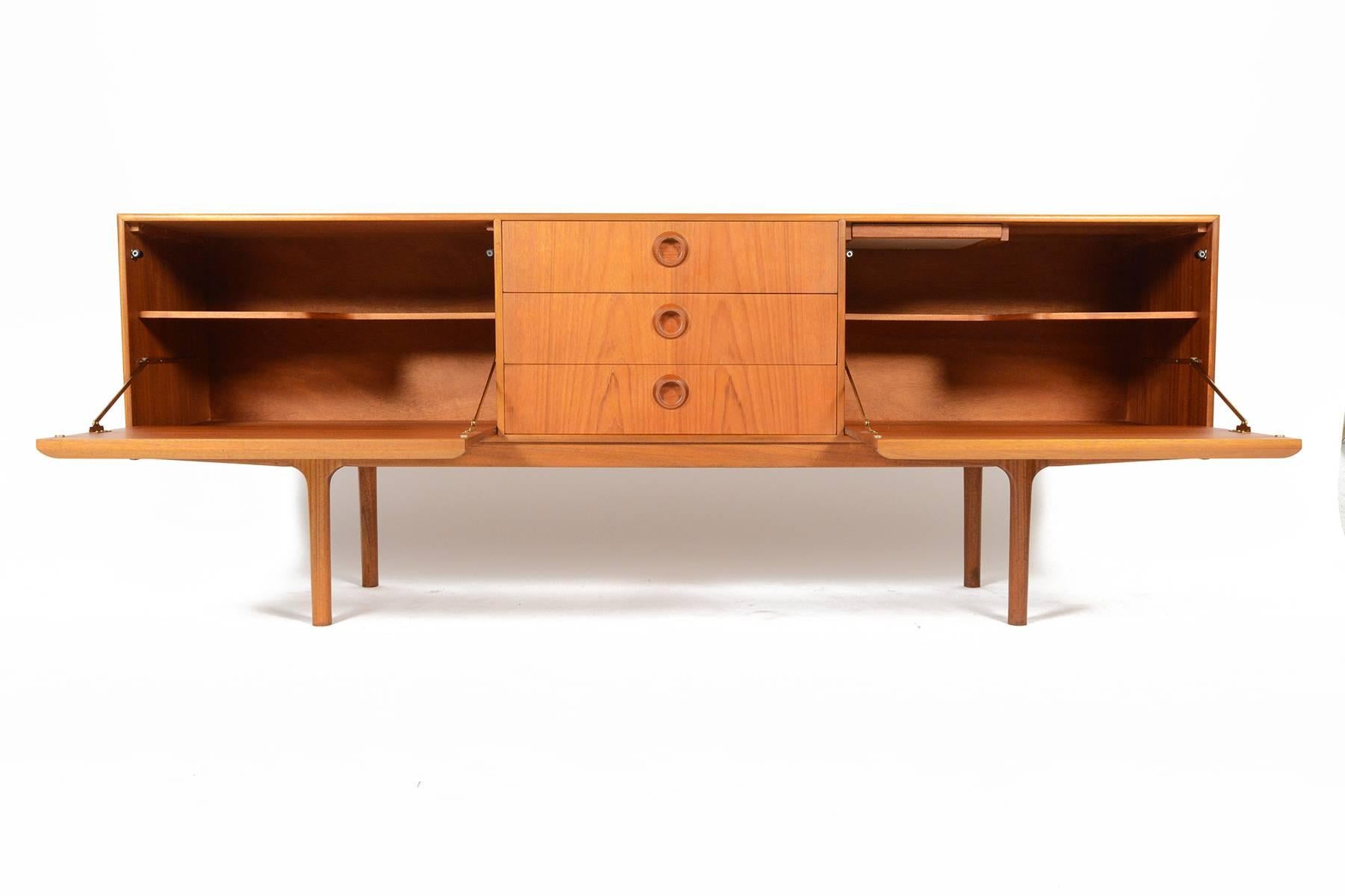 This rare large teak credenza was designed by A.H. McIntosh and offers a wonderful storage solution for any modern home. Left and right doors drop down revealing fixed shelves. Right cabinet features a pull- out black laminate tray, perfect for