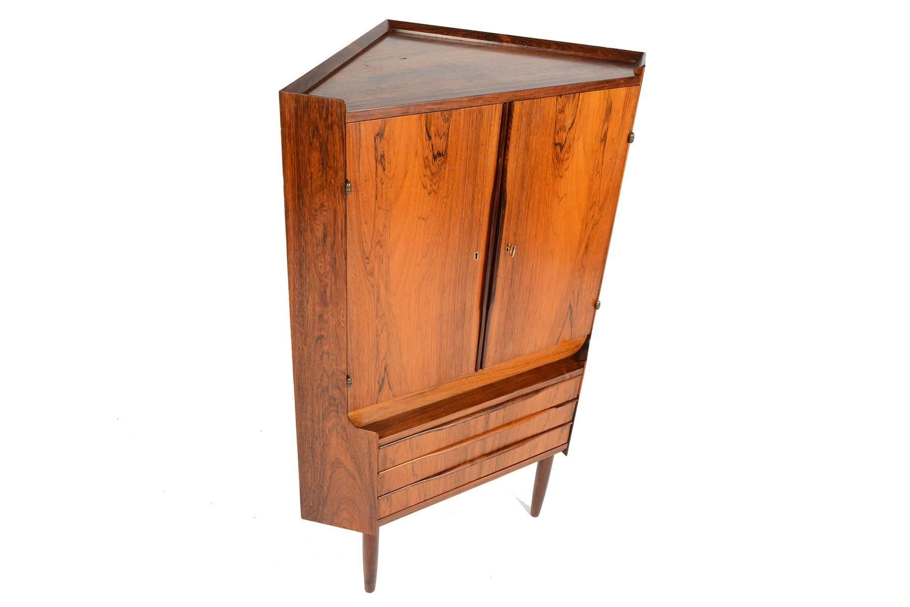 This Danish modern mid century corner cabinet and bar is perfect for any space with limited storage. Crafted in Brazilian rosewood, this piece will tuck easily into any corner of your home, providing you with a ready to use dry bar! Two top locking