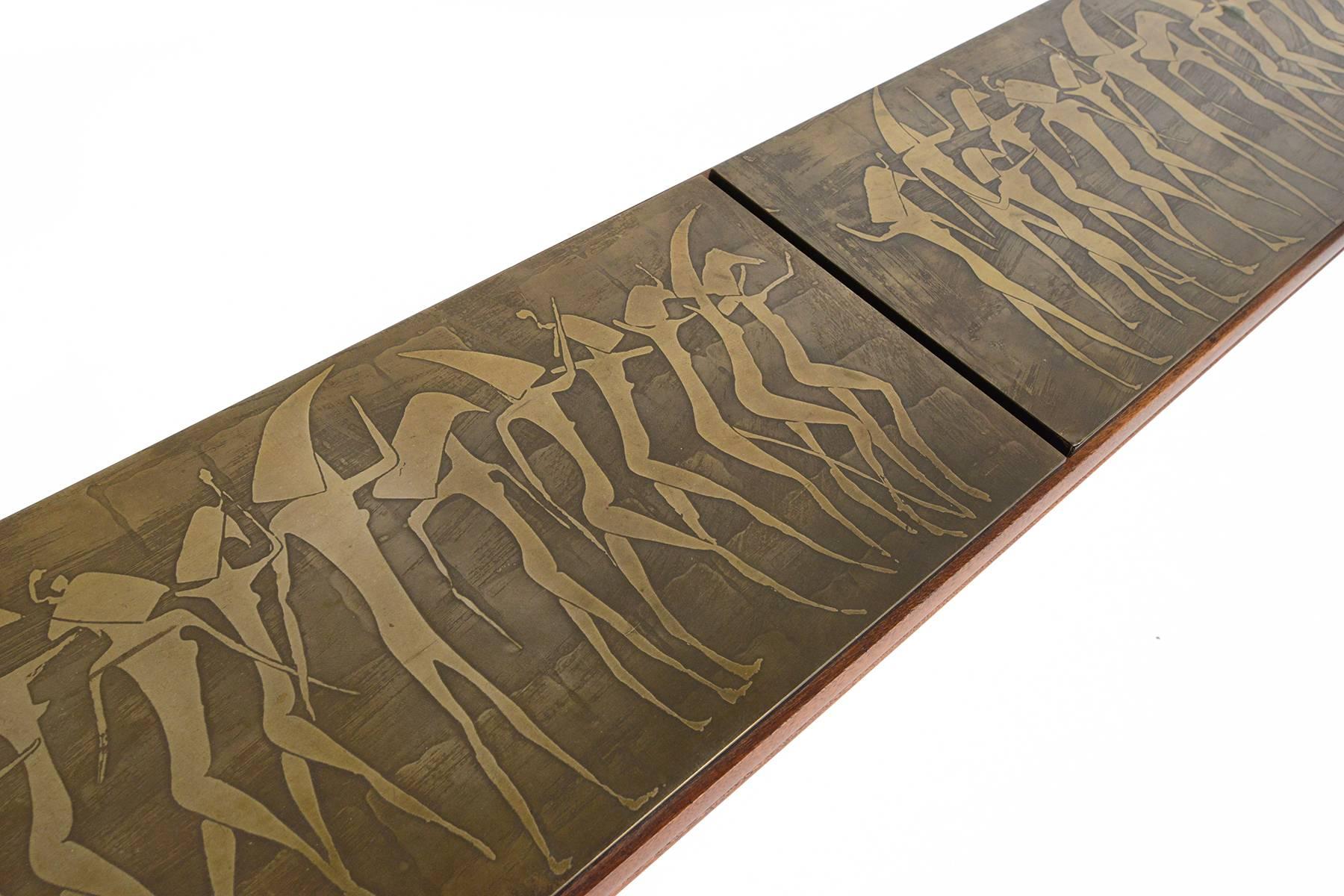 This rare and unusual walnut console table was crafted by Metropolitan Furniture in the 1960s. Four sculpted legs support this long table top. Three gilded brass panels depicting an abstract Egyptian relief adorn the top of this striking table. In