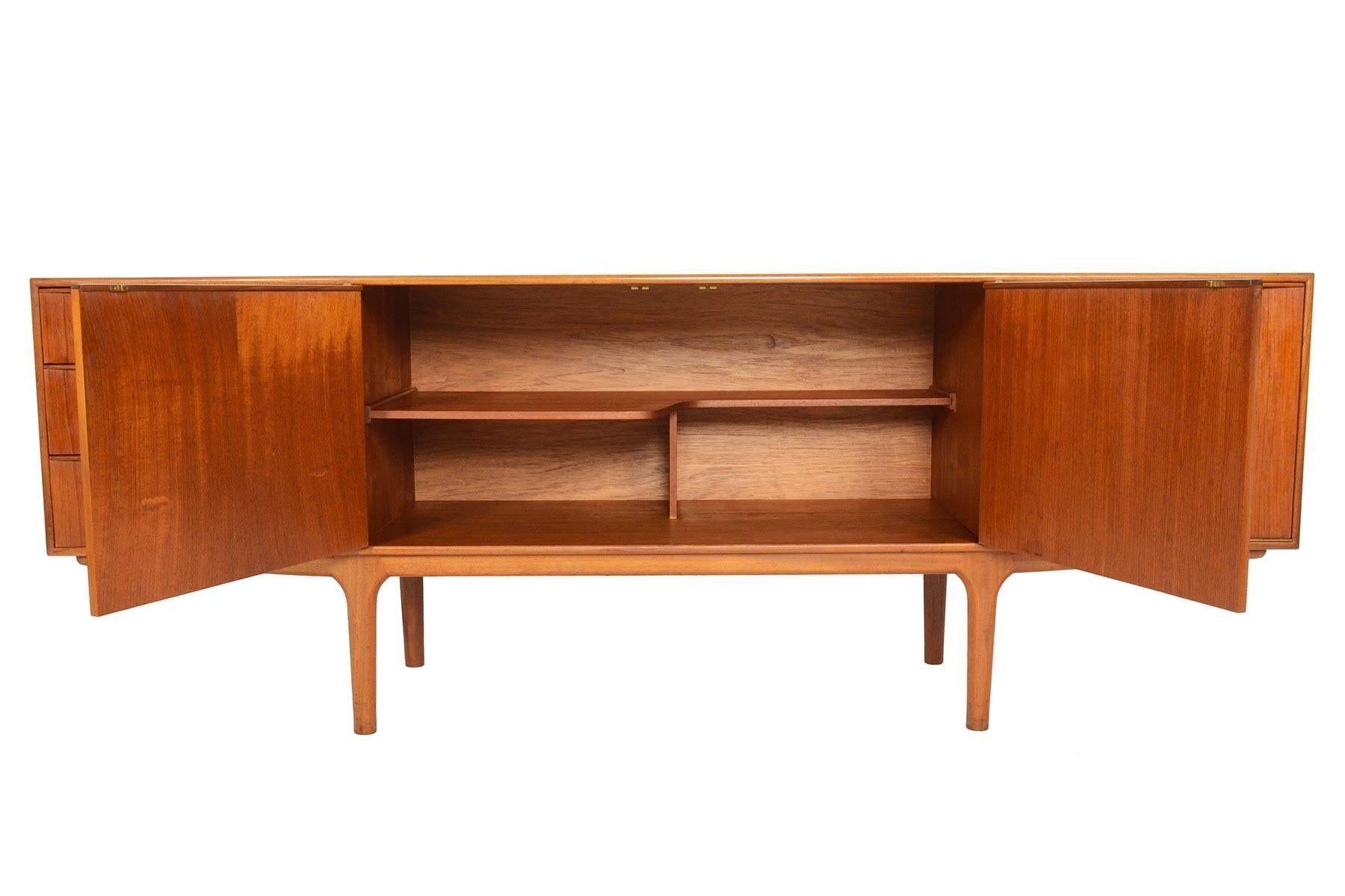 This Mid-Century Modern large low line teak sideboard by A.H. McIntosh is from the Dunvegan Range. Two centre doors open to reveal a fixed asymmetrical bar shelf. Right bar cabinet drops down to reveal open storage, and a slide out laminated drink