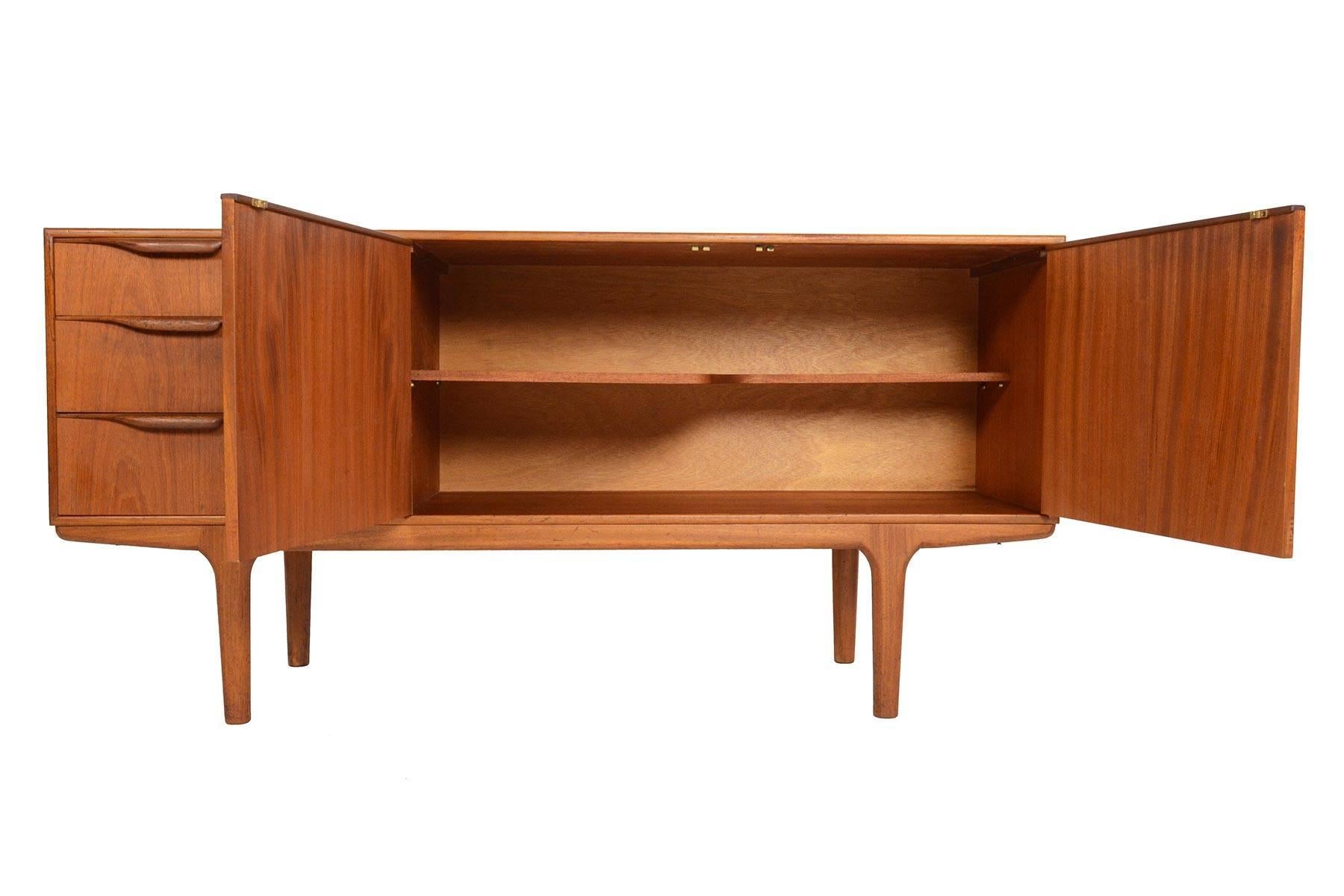This Mid-Century Modern low line teak sideboard by A.H. McIntosh was designed for the Dunvegan range. Two center doors open to reveal a fixed asymmetrical bar shelf. Three left oriented drawers provide additional storage for flatware and linens. In