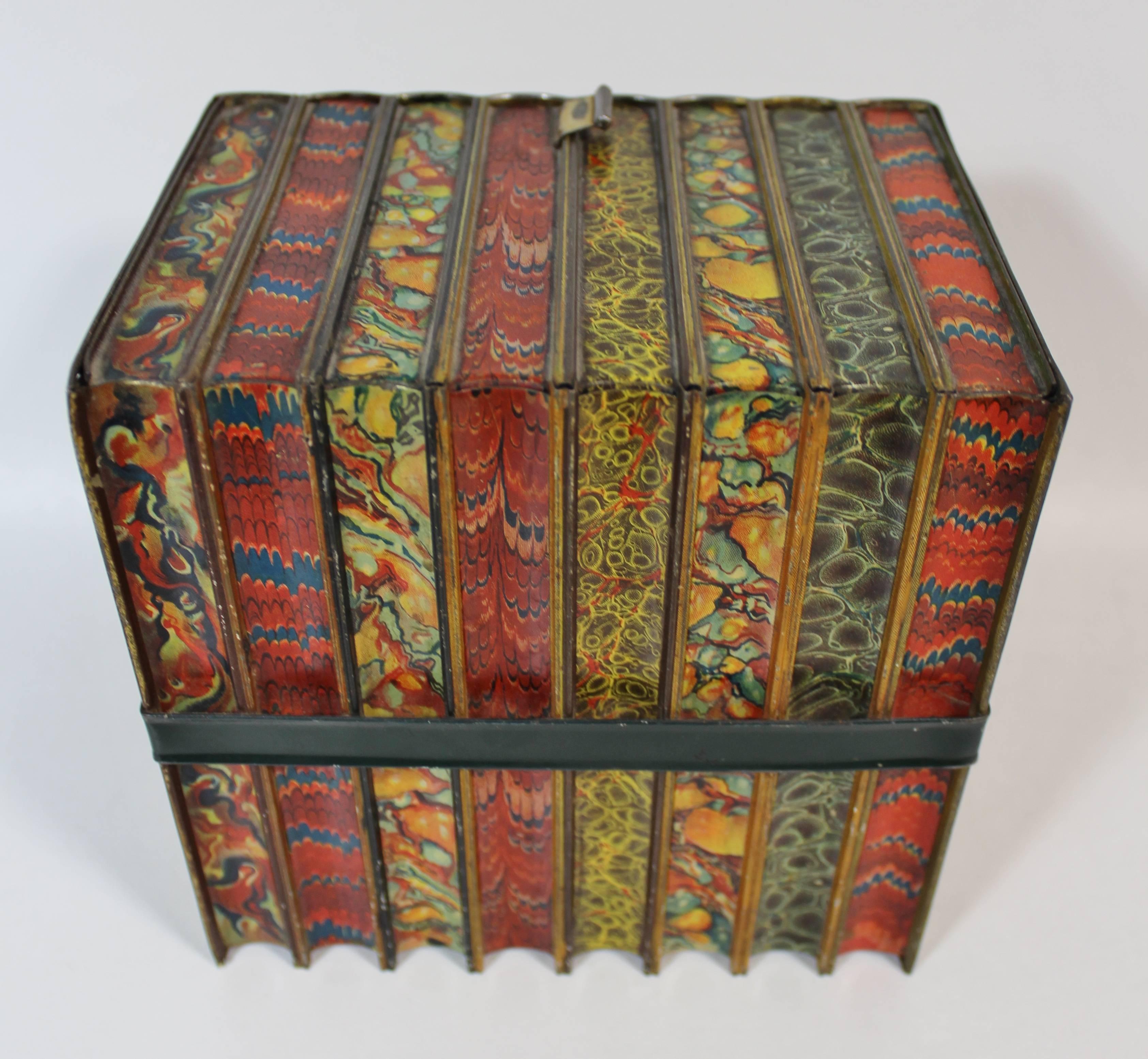 A Huntley & Palmers biscuit tin of the 'Literature' pattern, simulating a bundle of leather bound books with marbleized page ends. They're held together by a tin leather strap and a pull tab to open the tin box resembles a bookmark.