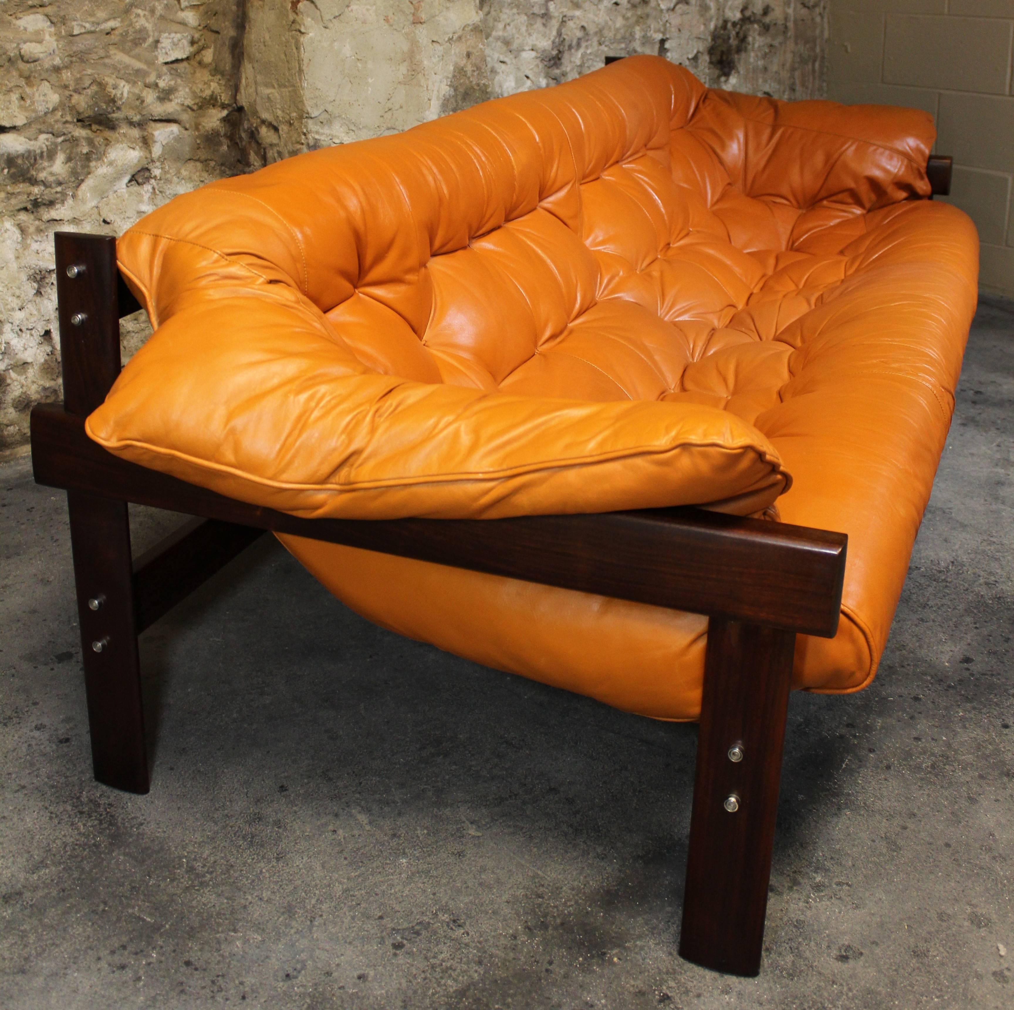 Absolutely stunning leather and jacaranda wood (Brazilian rosewood) sling sofa by iconic Brazilian designer Percival Lafer. Designed in the 1970s, this sofa features chrome accents, burnt orange tufted leather upholstery and an exotic rosewood frame