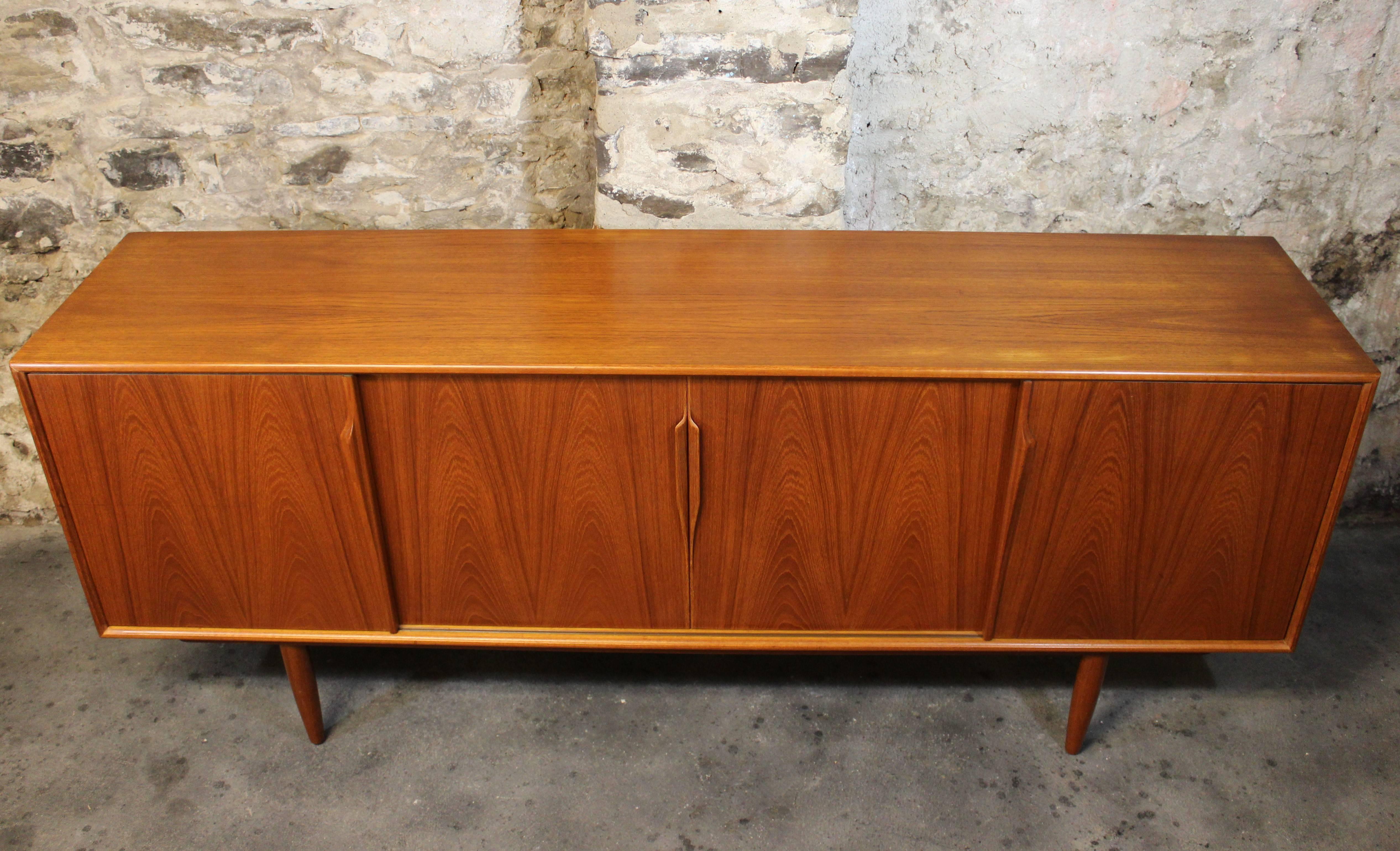 Solid teak credenza by Gunni Omann for Axel Christensen Odder. This fabulous example has sculptural solid teak handles with subtly tapered solid teak legs. The middle of the chest has three dovetailed pull-out drawers while the left and right sides